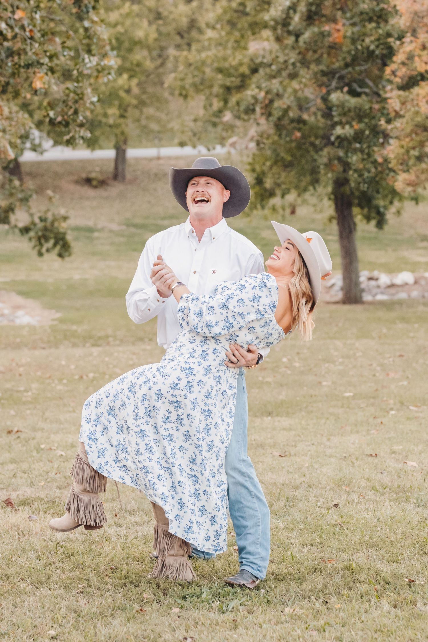 Couple in western wear share romantic dance pose outdoors under autumn trees.