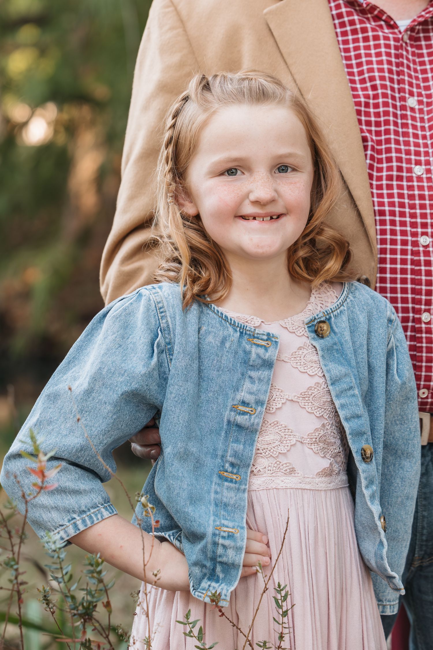 Close up portrait wearing denim jacket and pink dress against natural outdoor backdrop.