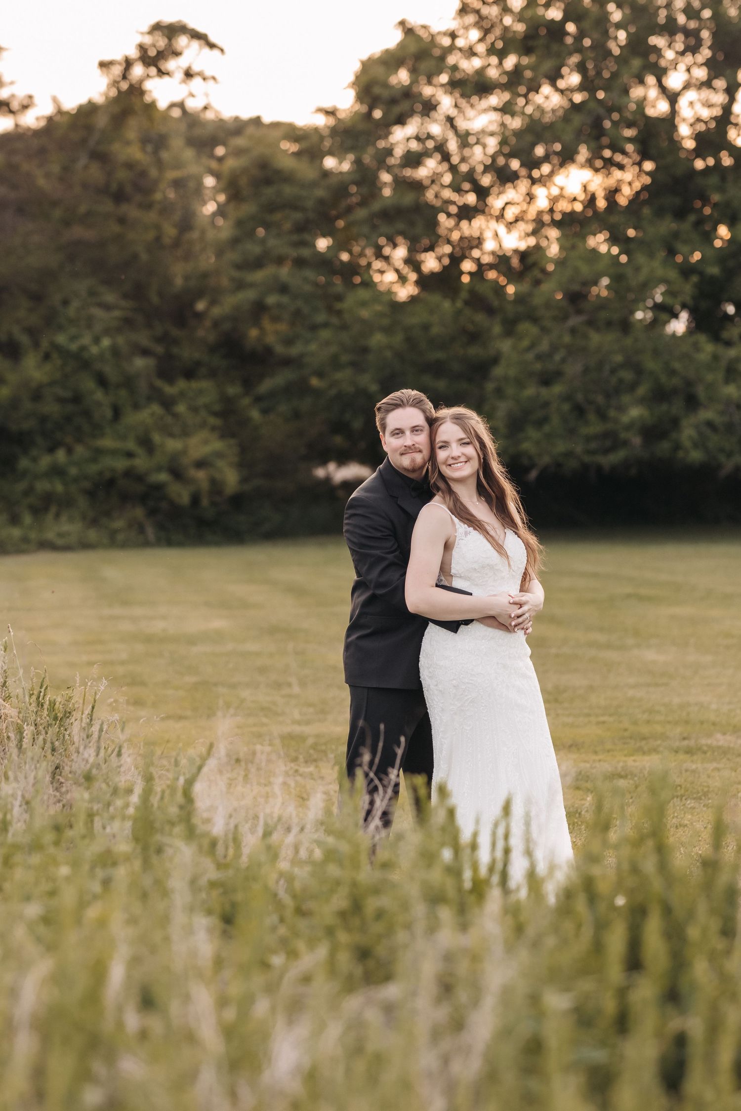 A loving couple poses for wedding photos in a rustic field during golden hour.