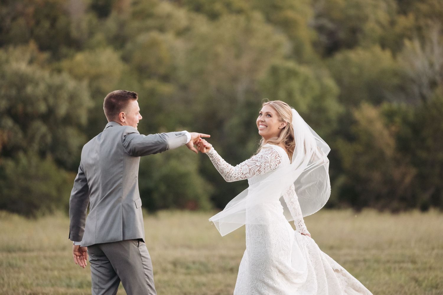 Joyful couple dances and spins in outdoor field during wedding celebration.