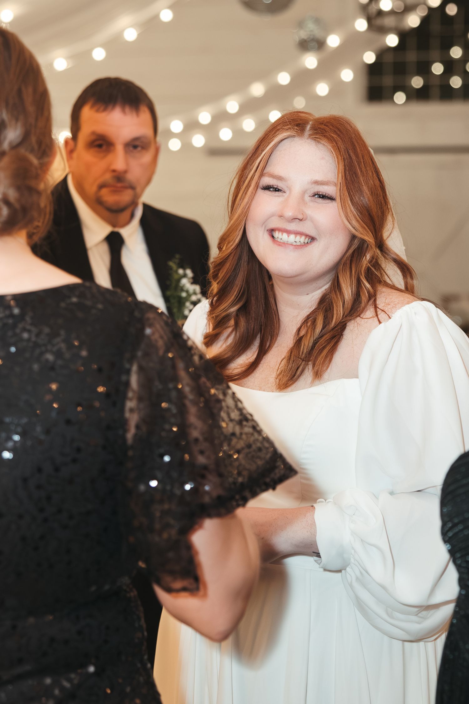 A festive wedding reception scene with decorative string lights and guests in formal attire.