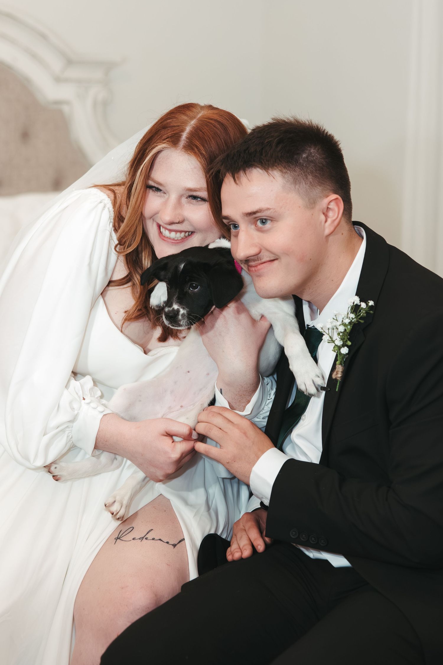 A happy couple in wedding attire poses with their small black dog.
