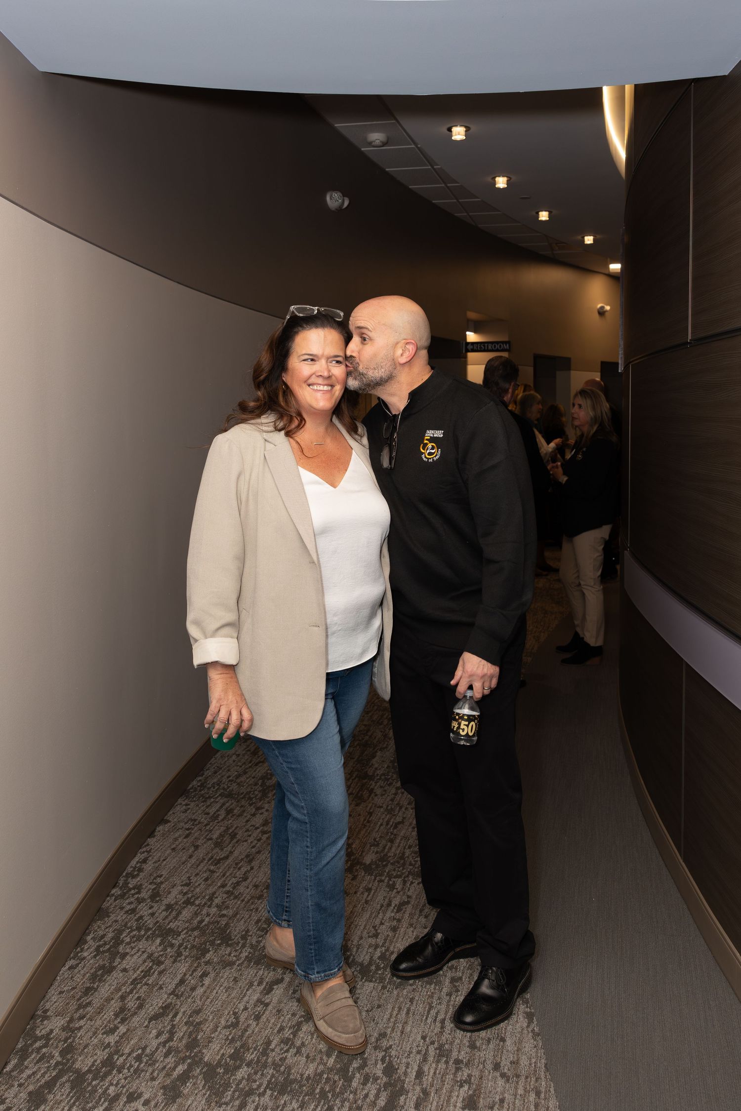 A couple standing together in a modern office corridor with recessed lighting.