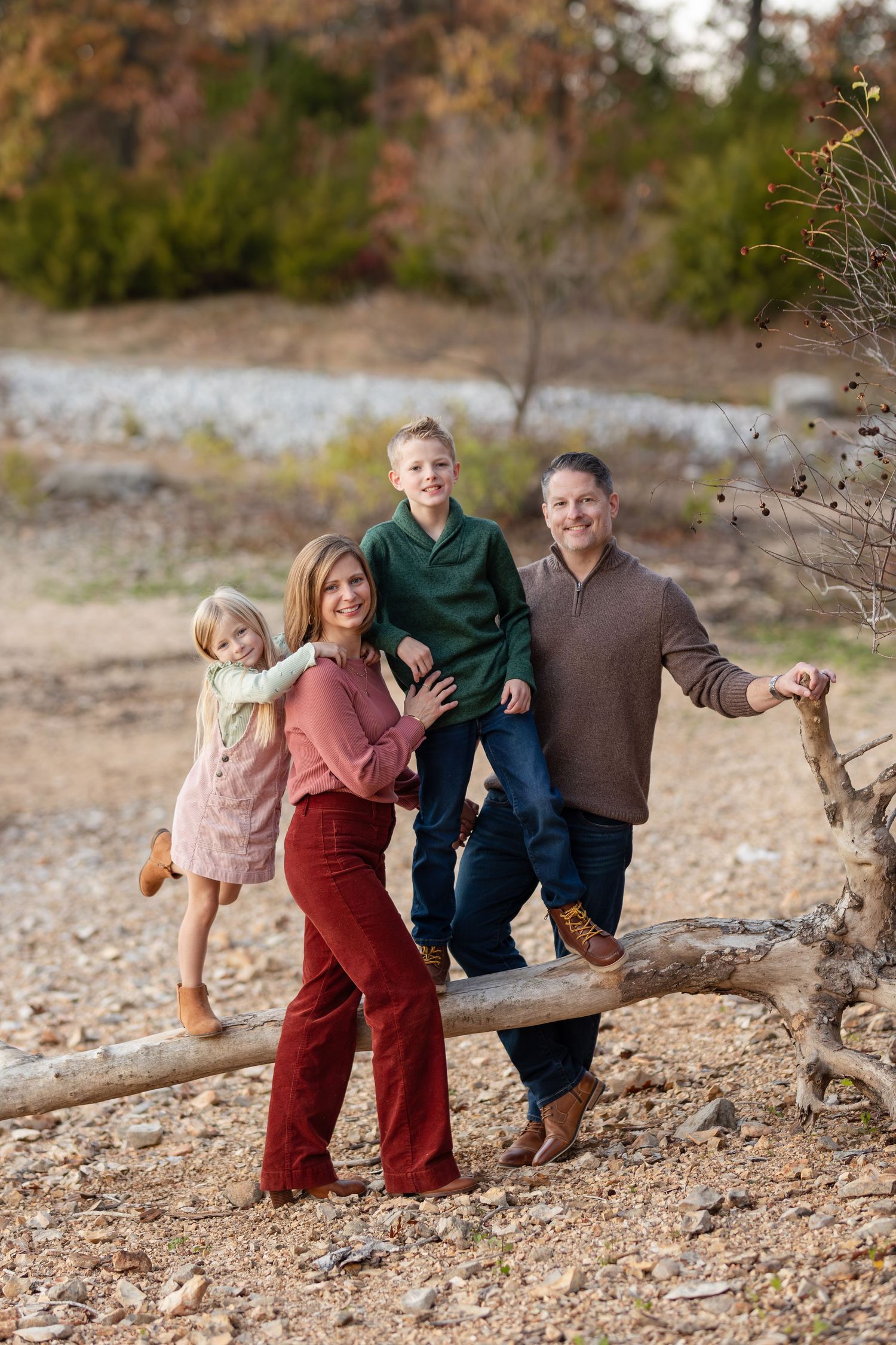 Family playfully posing on fallen tree trunk in natural outdoor setting during autumn.