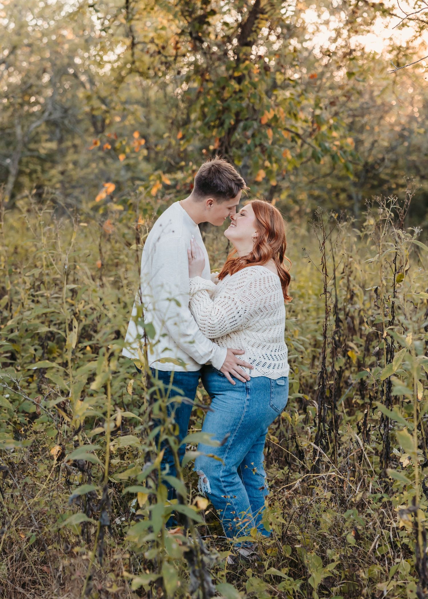 Romantic couple embracing among tall grass during sunset.
