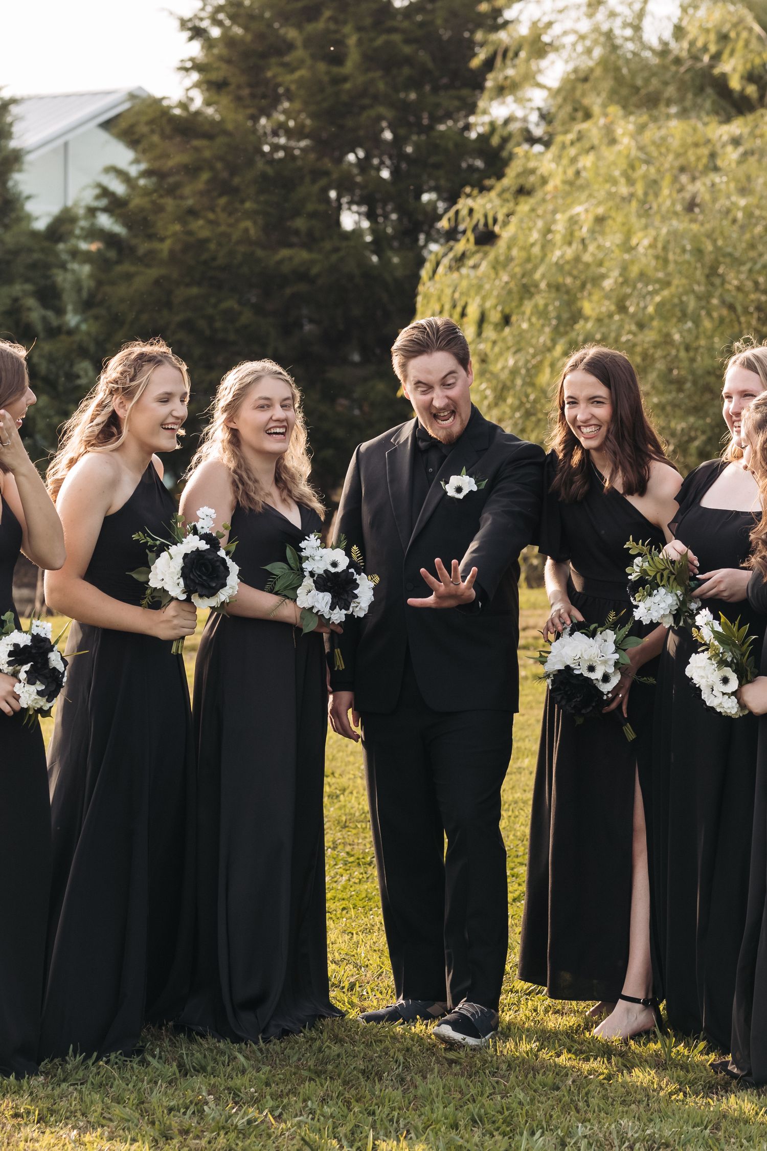 Wedding party in elegant black attire shares a candid moment outdoors.
