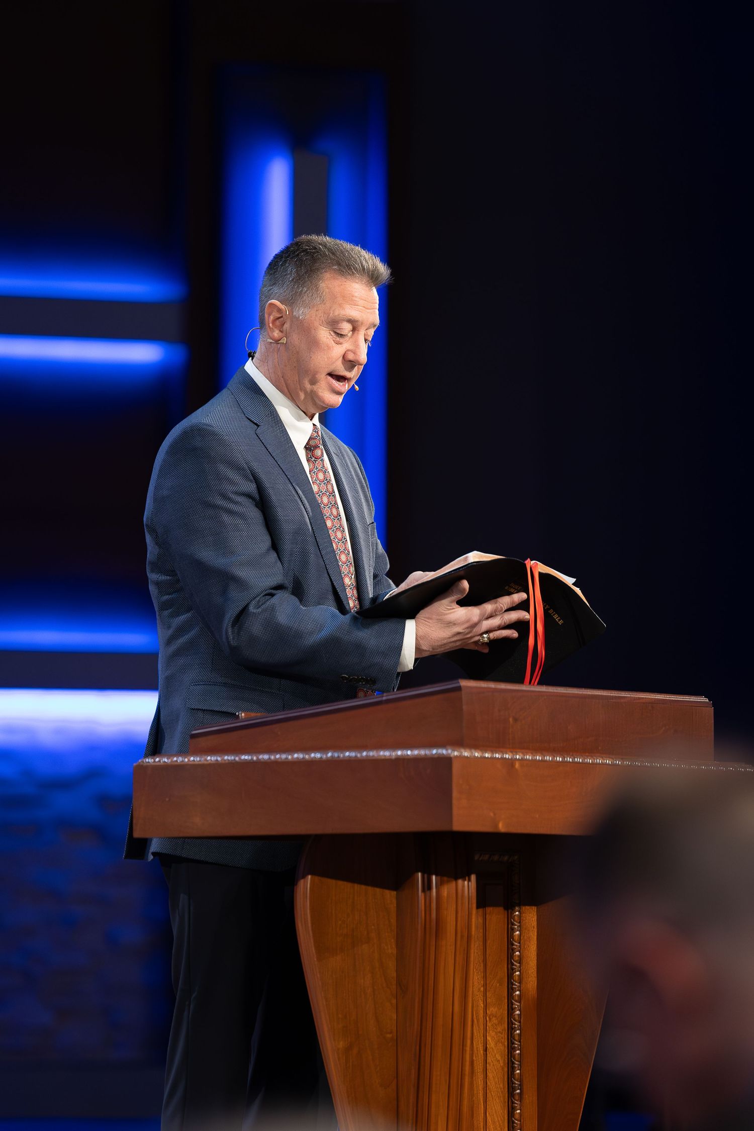 Minister delivers sermon from wooden pulpit with blue lighting effects.