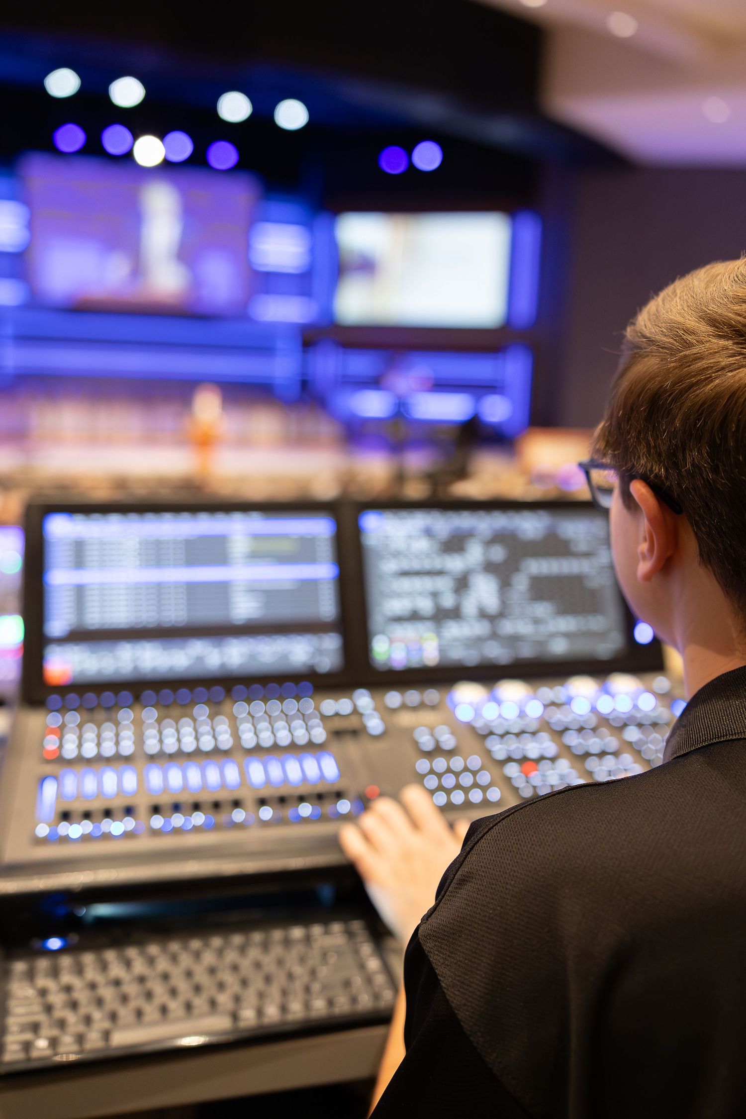 Audio technician operating a professional sound mixing board with blue lighting in background.