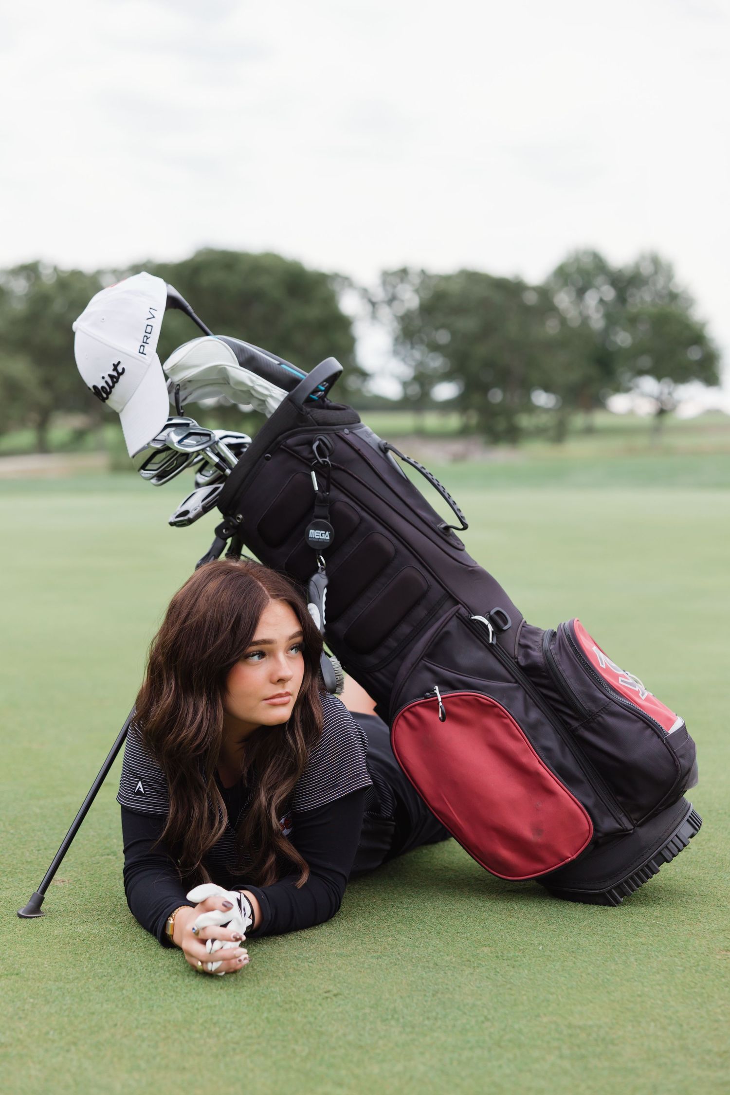 A golfer lies on the manicured grass while wearing dark clothing next to a golf bag on the course.