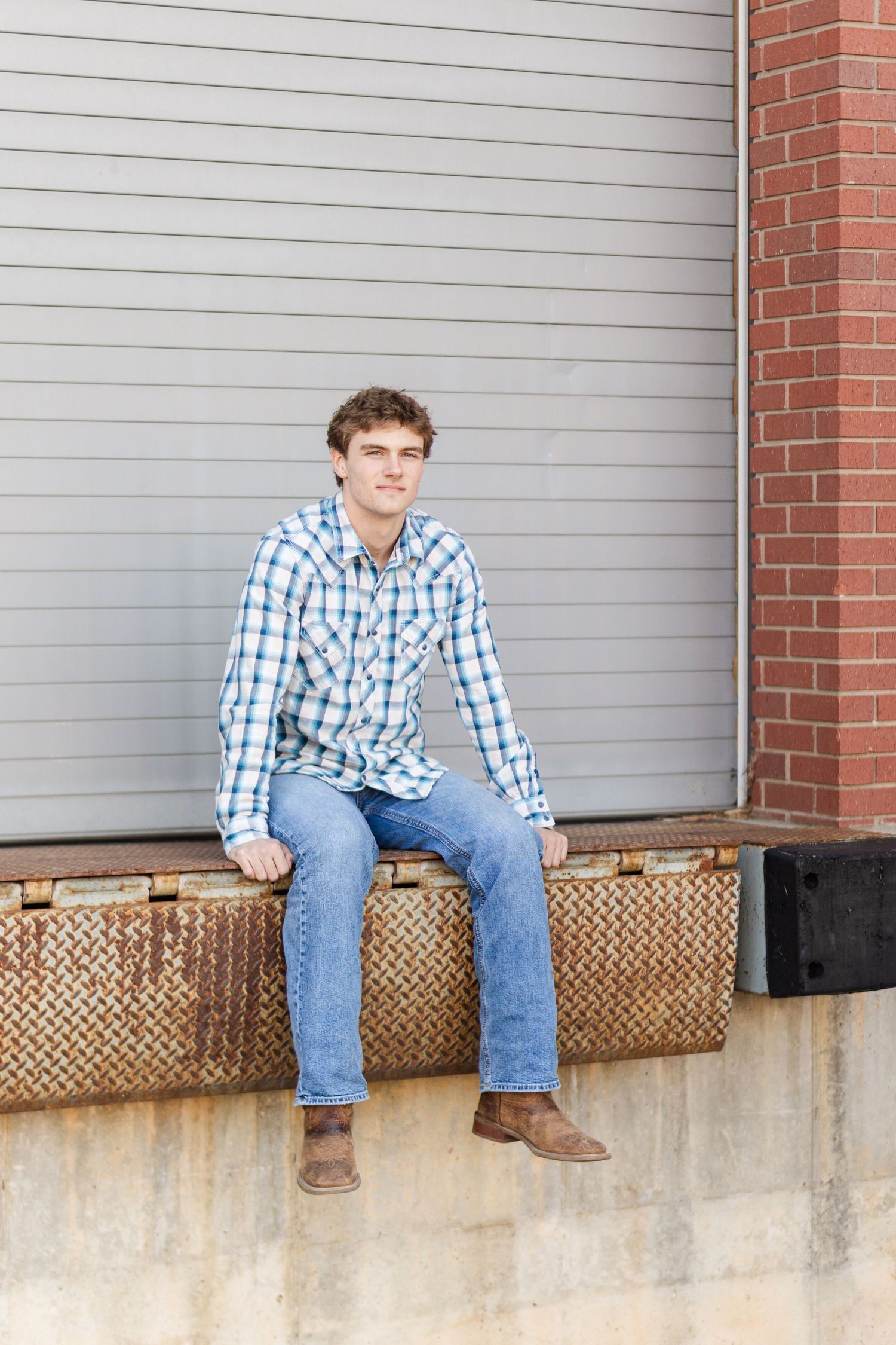 Person sitting on concrete ledge against gray wall wearing plaid shirt and jeans.