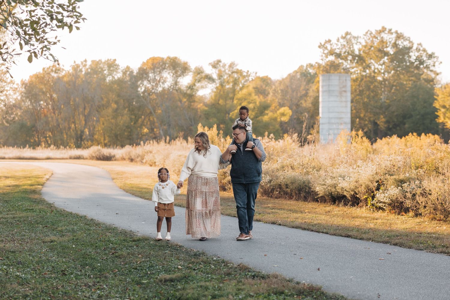 Family walking together on a paved path through a golden autumn park.
