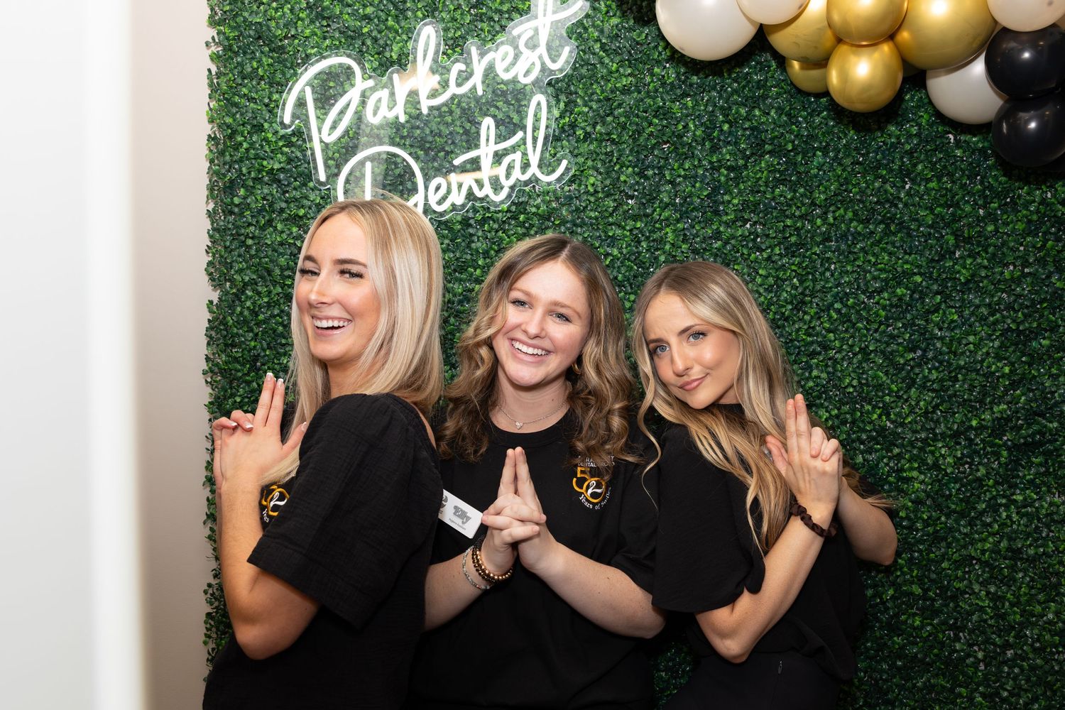 Staff members pose in black uniforms against a decorative green wall with neon signage.