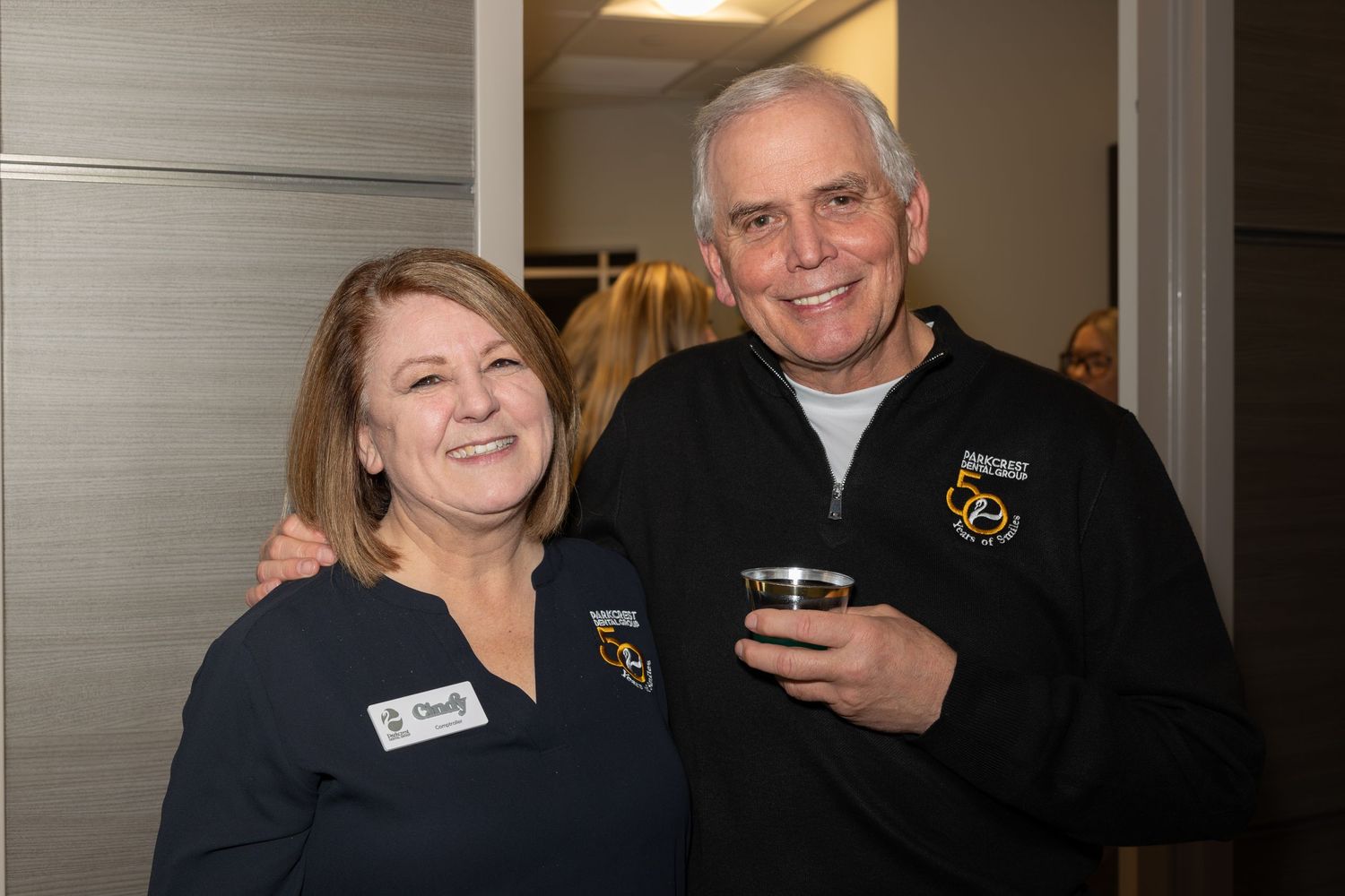Two staff members wearing branded uniforms smiling together at an office celebration.