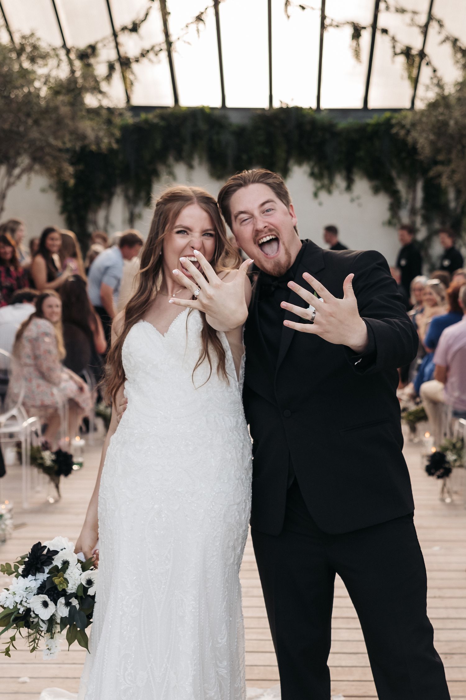 Newlyweds showing excitement and displaying rings during wedding ceremony in indoor venue.