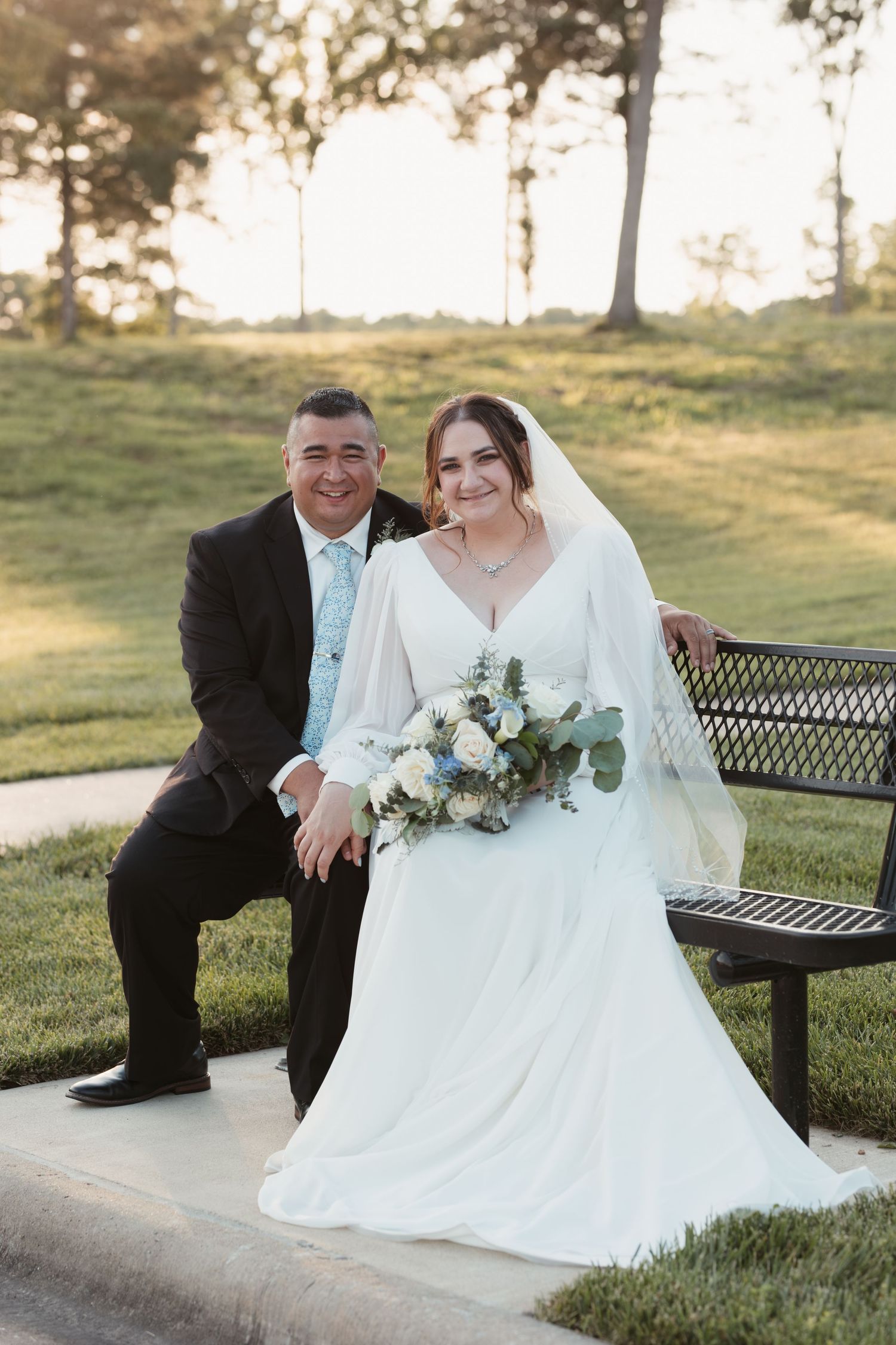Newlyweds pose together on bench during outdoor sunset photo session.