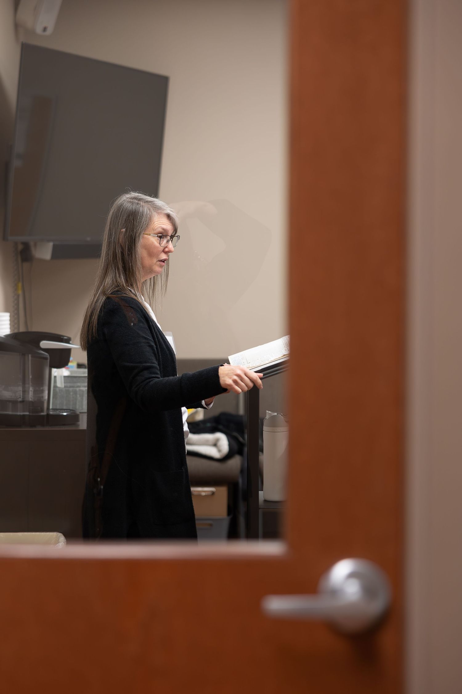 Person in black attire reading a book in an office setting.