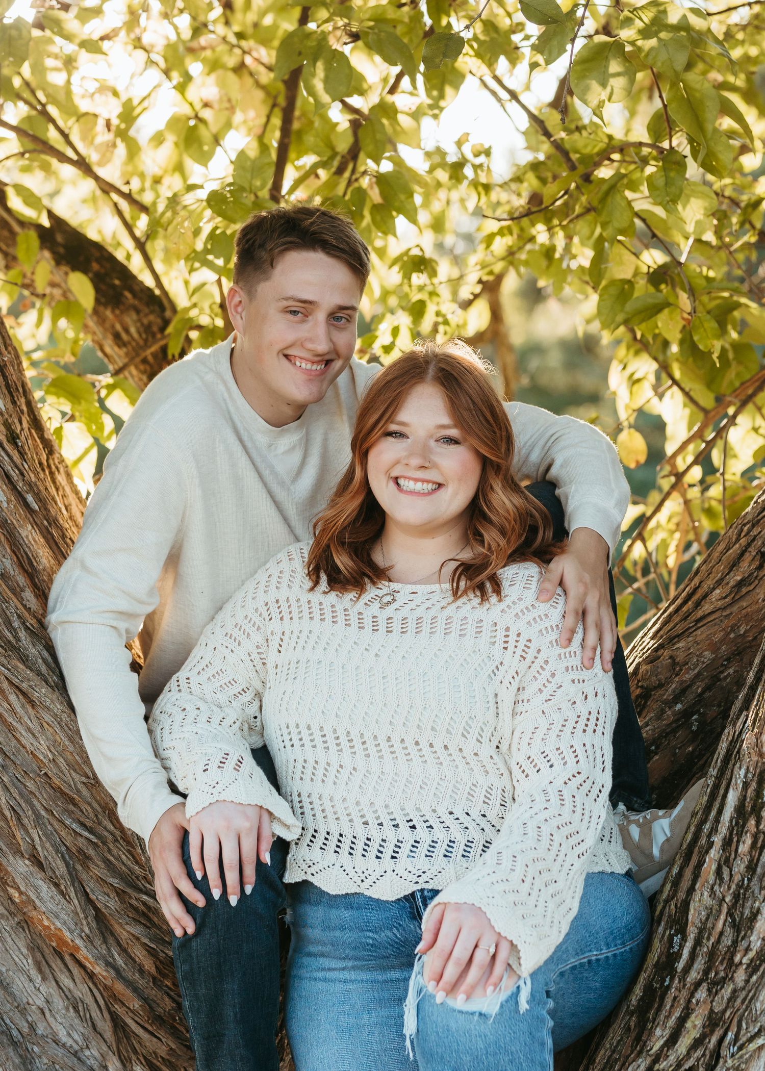 A couple shares a happy moment while sitting in a tree during an autumn photoshoot.