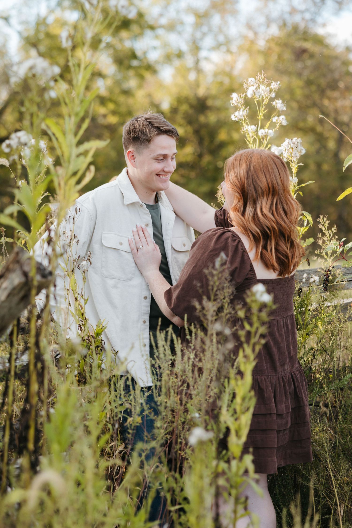 Couple laughing together in a field of white wildflowers during golden hour.