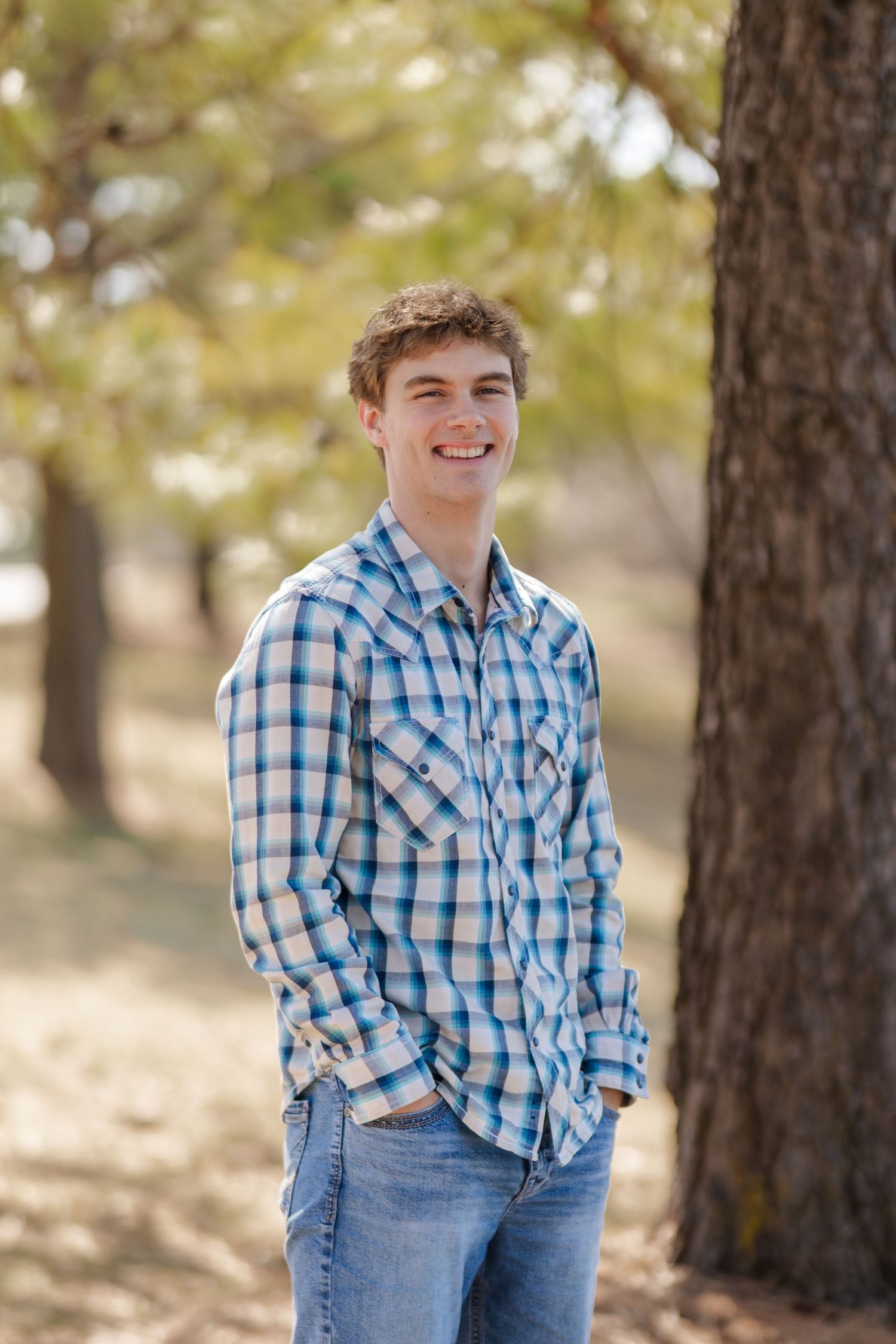 Casual outdoor portrait in blue plaid shirt against autumn trees.