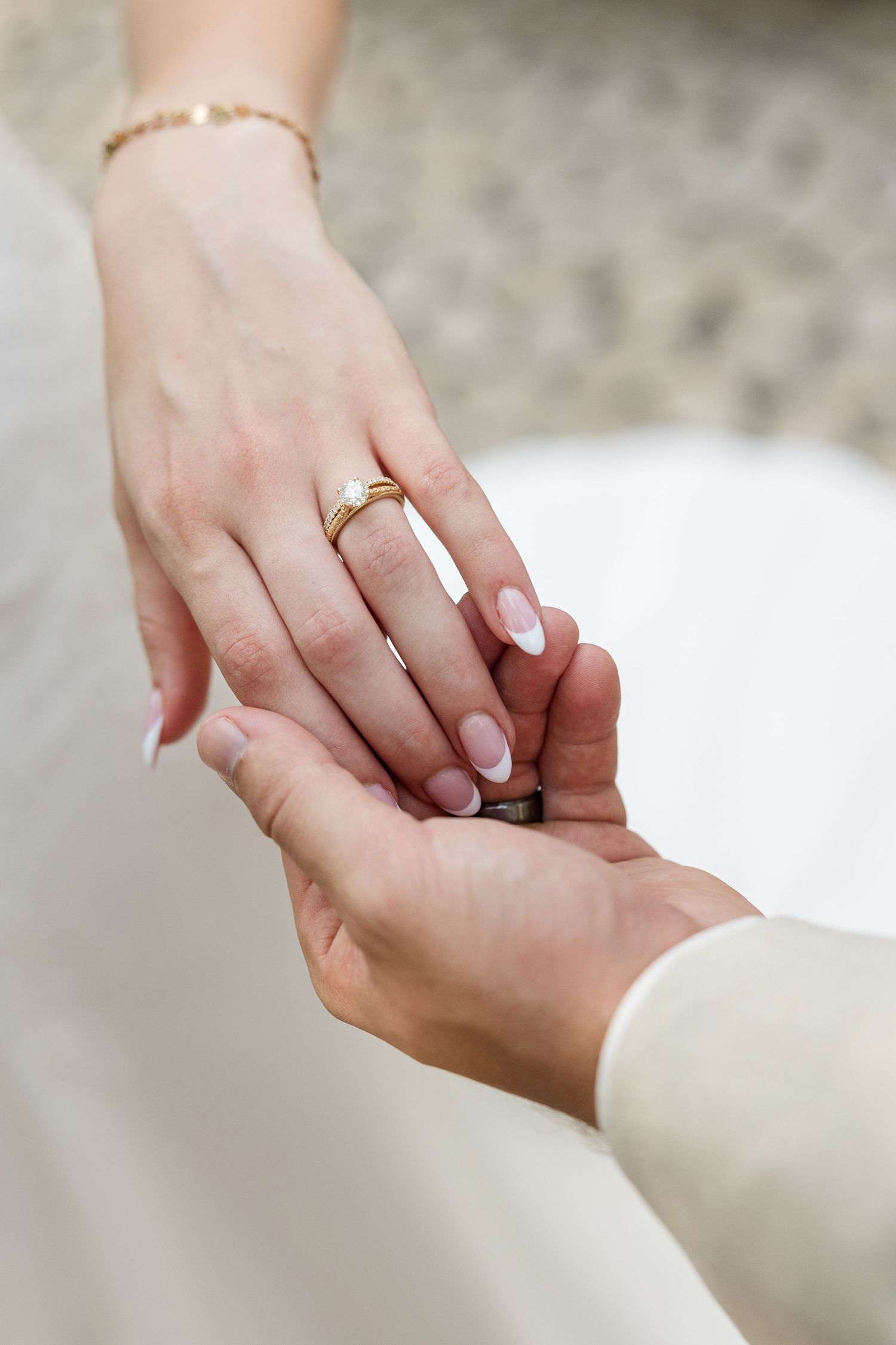 Groom placing a gold diamond engagement ring on bride's finger during wedding ceremony, with French manicure nails.