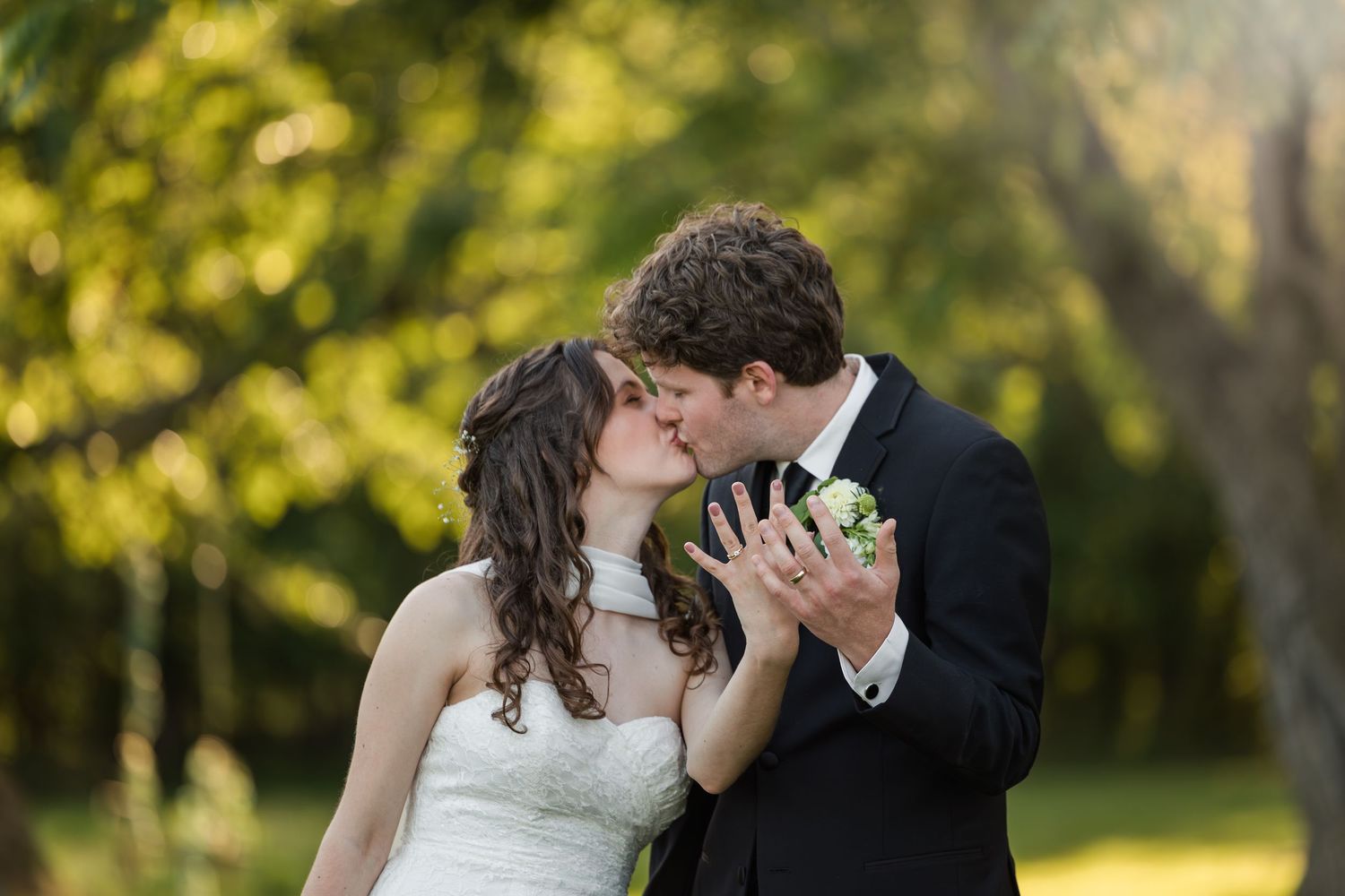 Bride and groom sharing a romantic kiss outdoors surrounded by lush green trees on their wedding day.