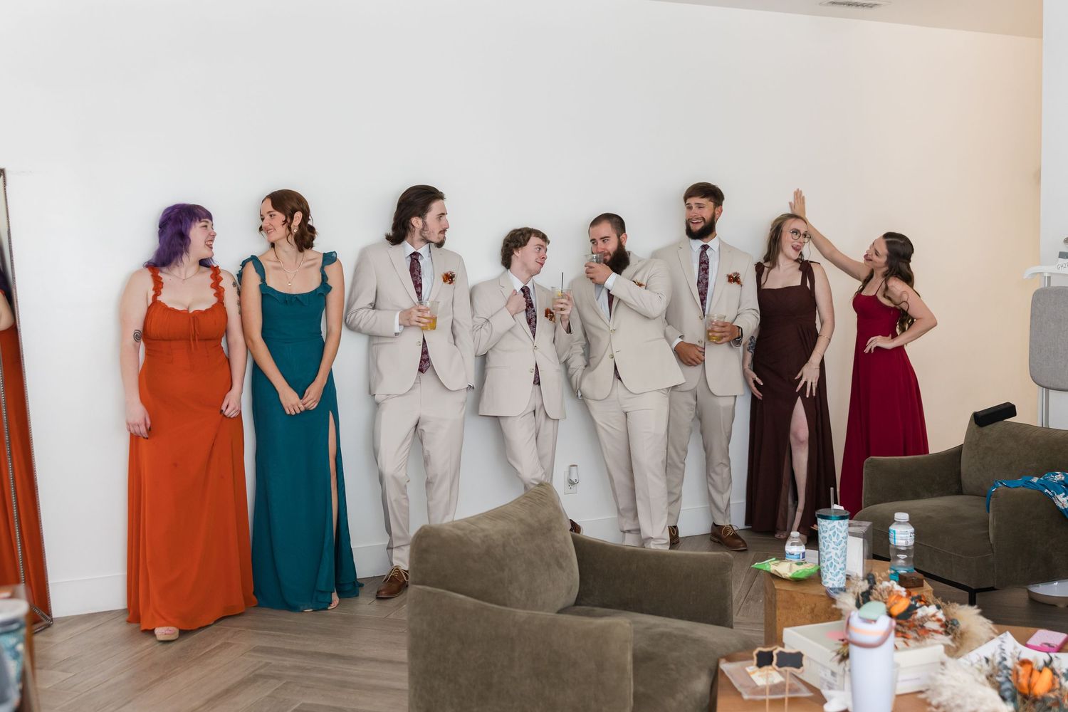 Wedding party in colorful formal attire posing together indoors with bridesmaids and groomsmen.