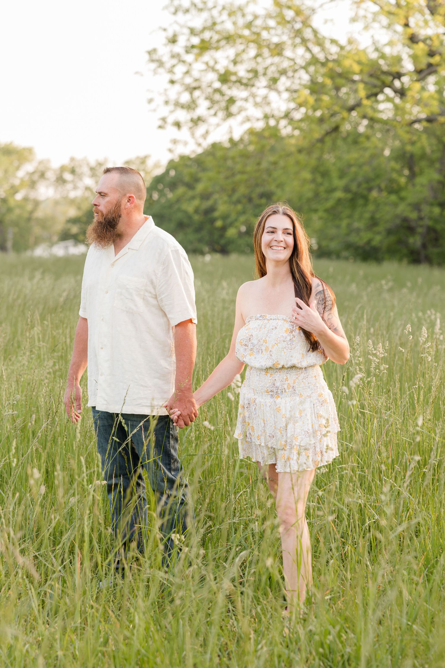 Couple walking together through a tall grass meadow on a sunny summer evening.