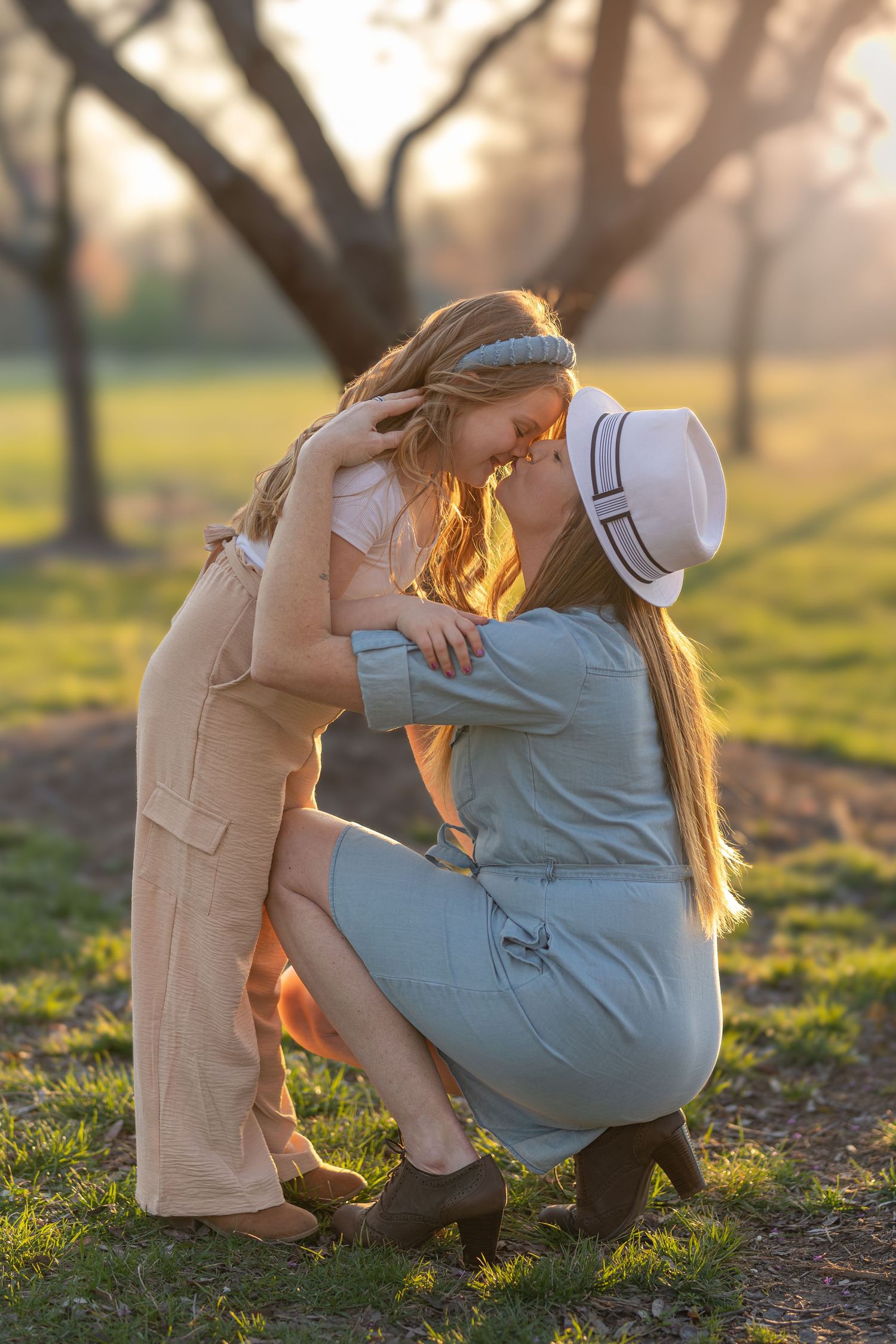 Mother and daughter share a tender moment together outdoors at sunset in a park with soft golden lighting.
