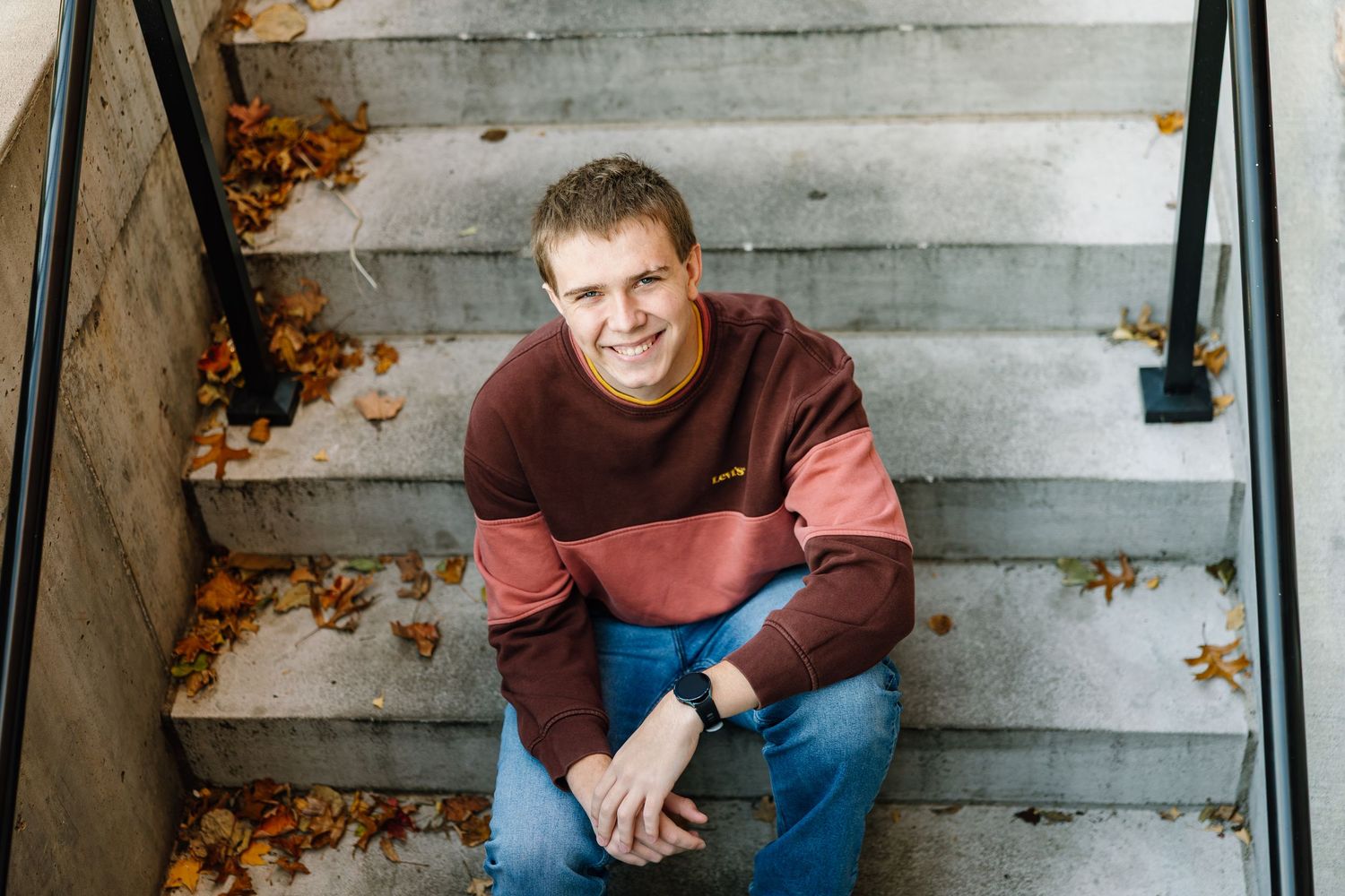 A person in a burgundy sweater sits on concrete steps covered with autumn leaves.
