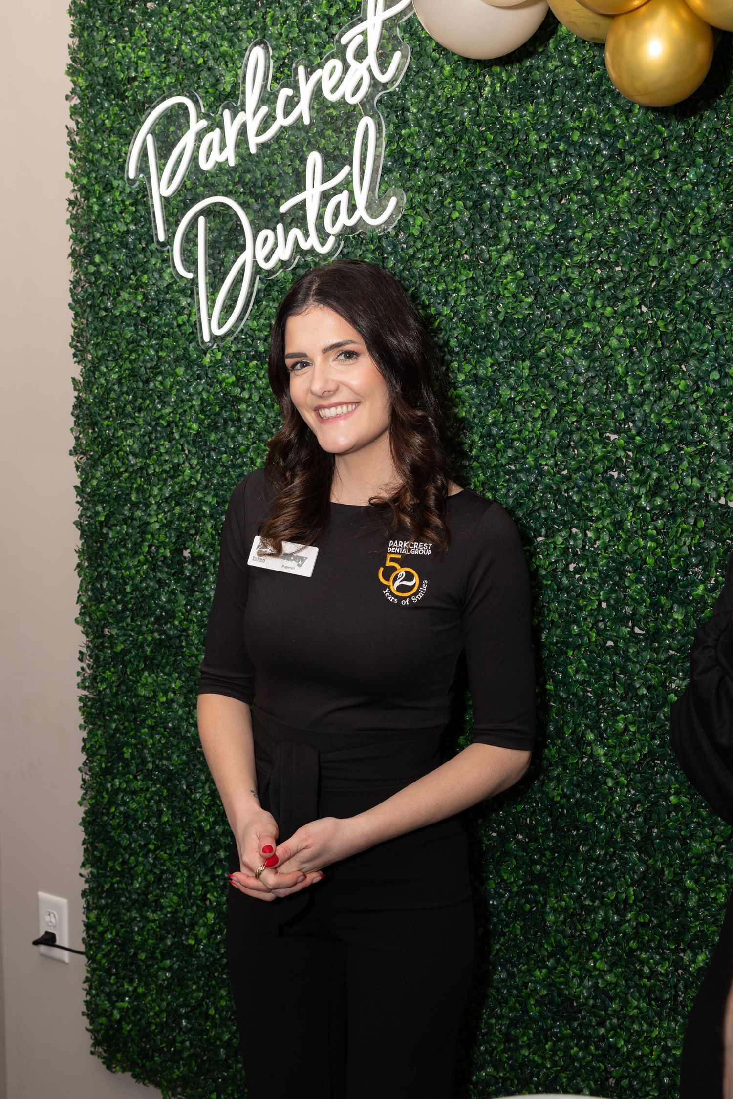 Staff member poses against green wall backdrop with Parkwest Dental signage and gold balloons.