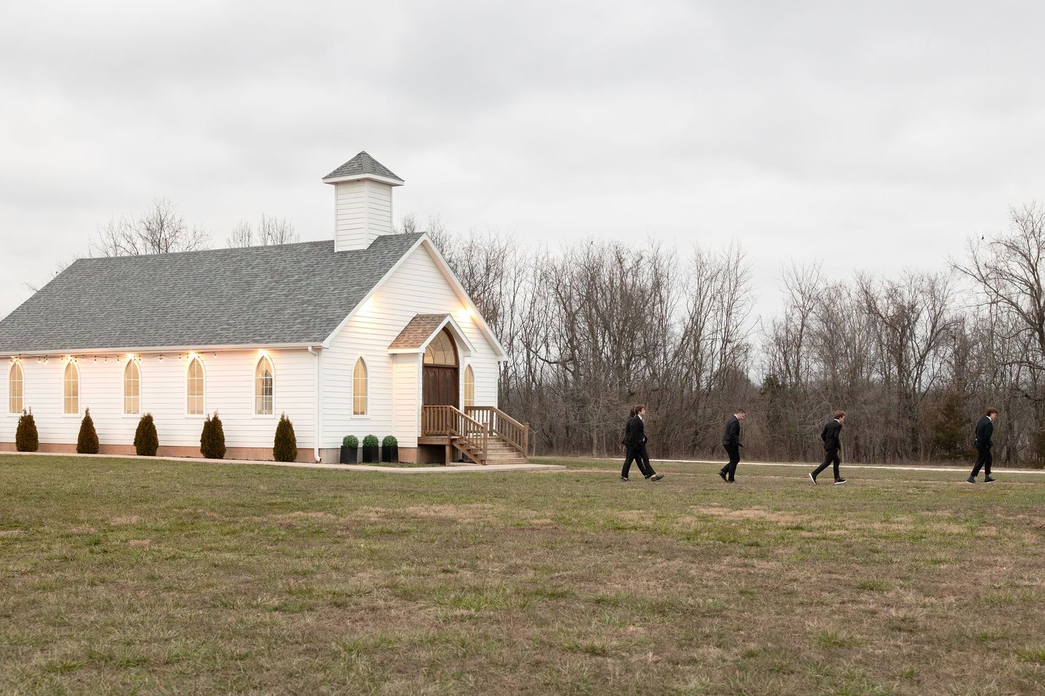 Silhouettes walking across field towards white chapel building in overcast weather.