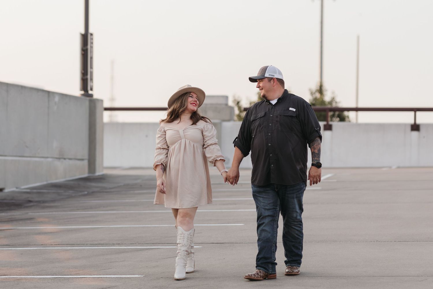 A couple walking hand in hand across an empty rooftop parking area at dusk.