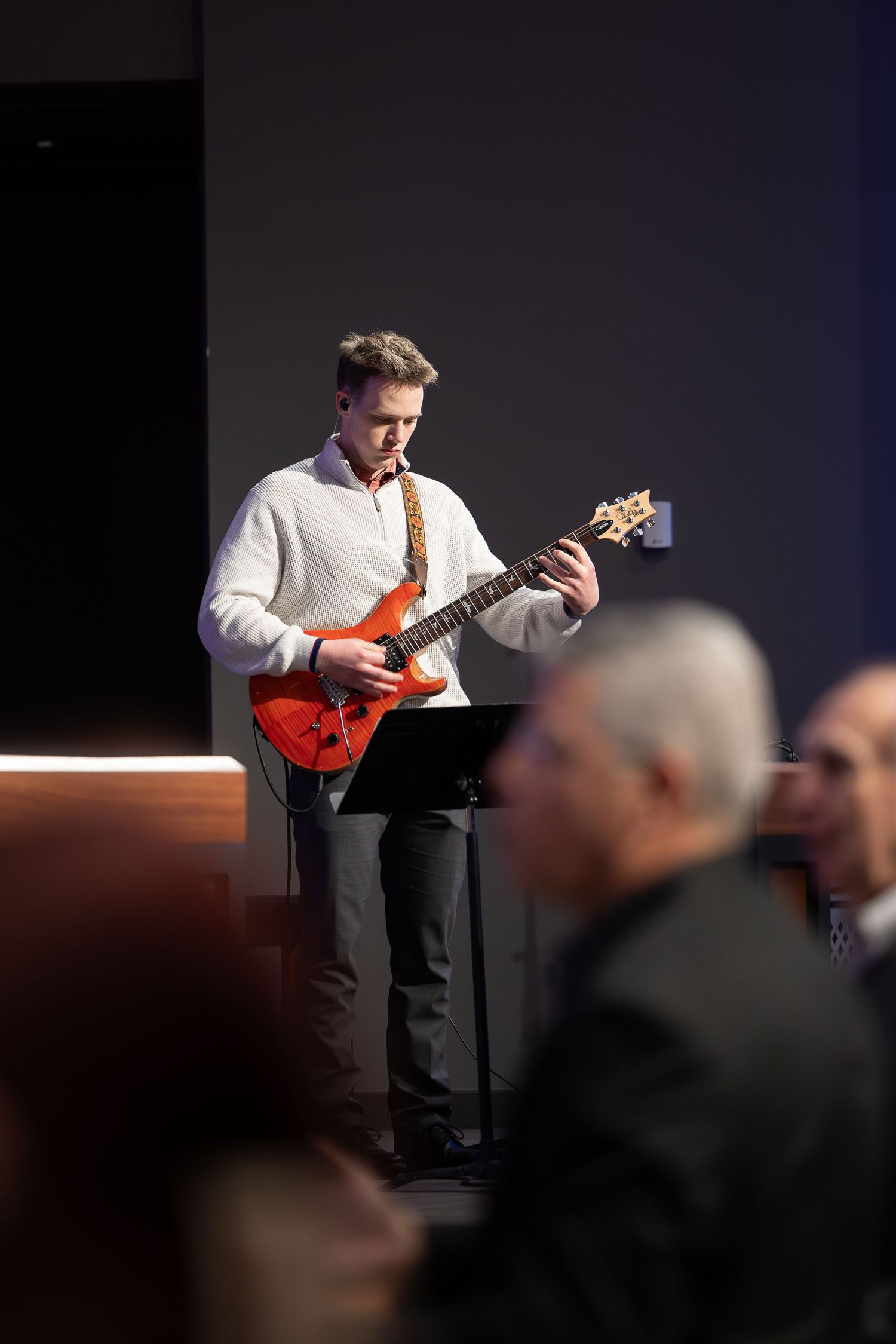 A guitarist performing on stage with red electric guitar in spotlight.