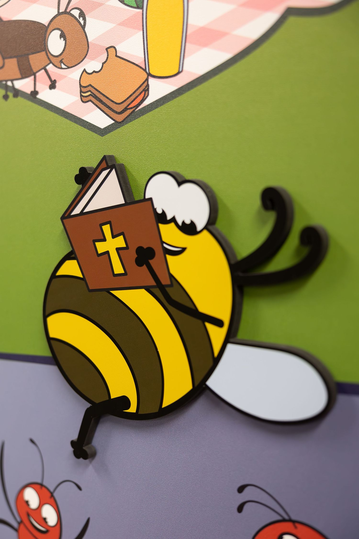 Cartoon bee character reading a bible book displayed on a colorful wall mural.