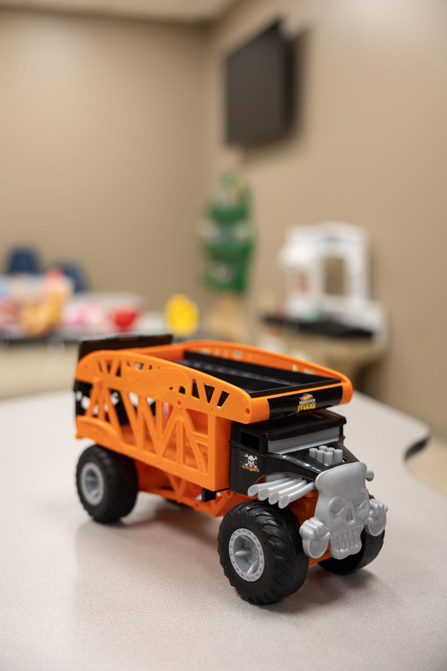 Orange toy monster truck with large wheels sits on a beige table surface.