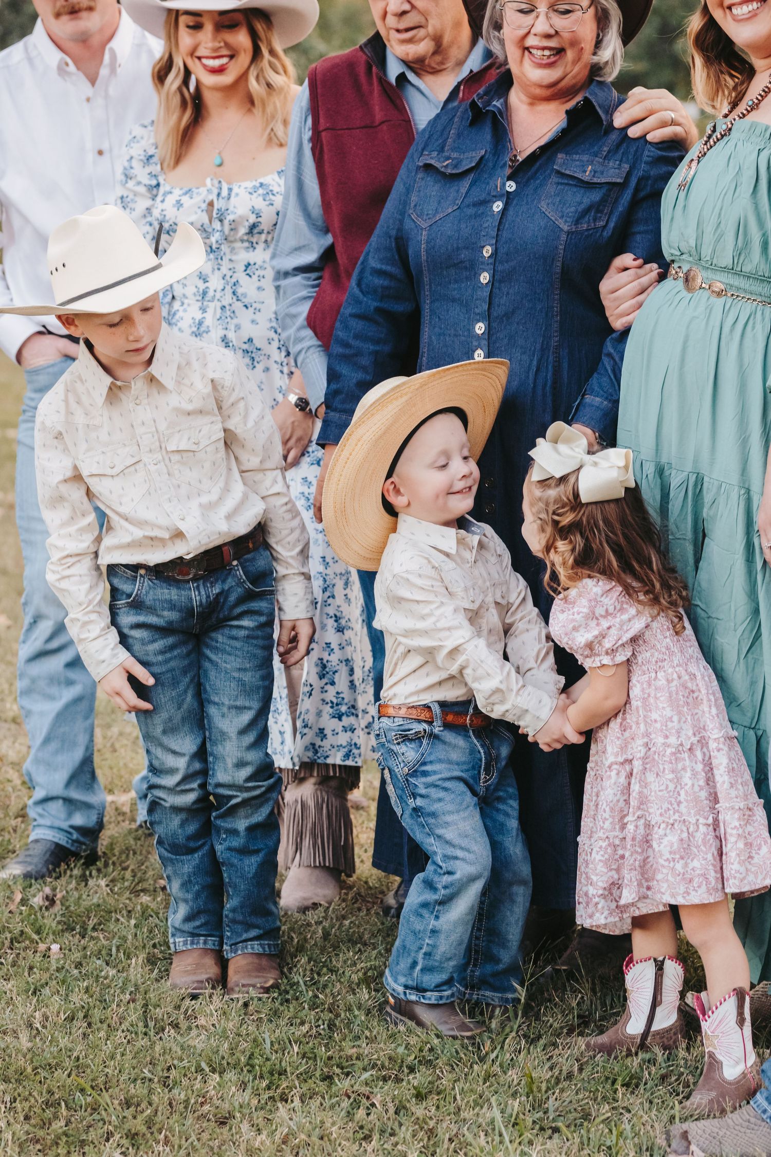 Multi-generational family in western attire poses together outdoors with children in cowboy hats.