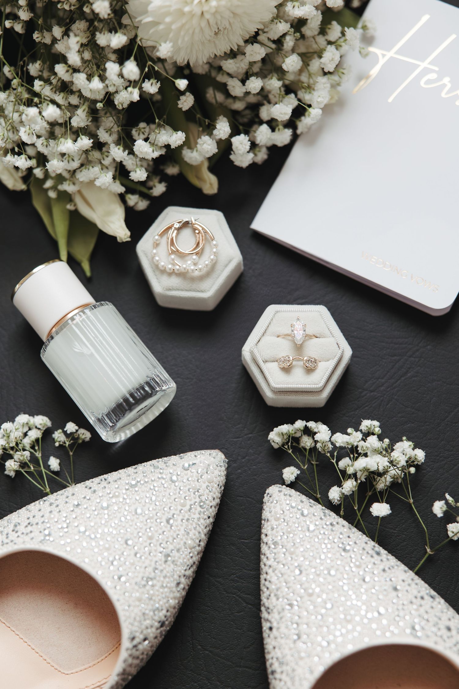 Elegant wedding accessories including beaded flats, baby's breath flowers, and hexagonal ring boxes on dark background.