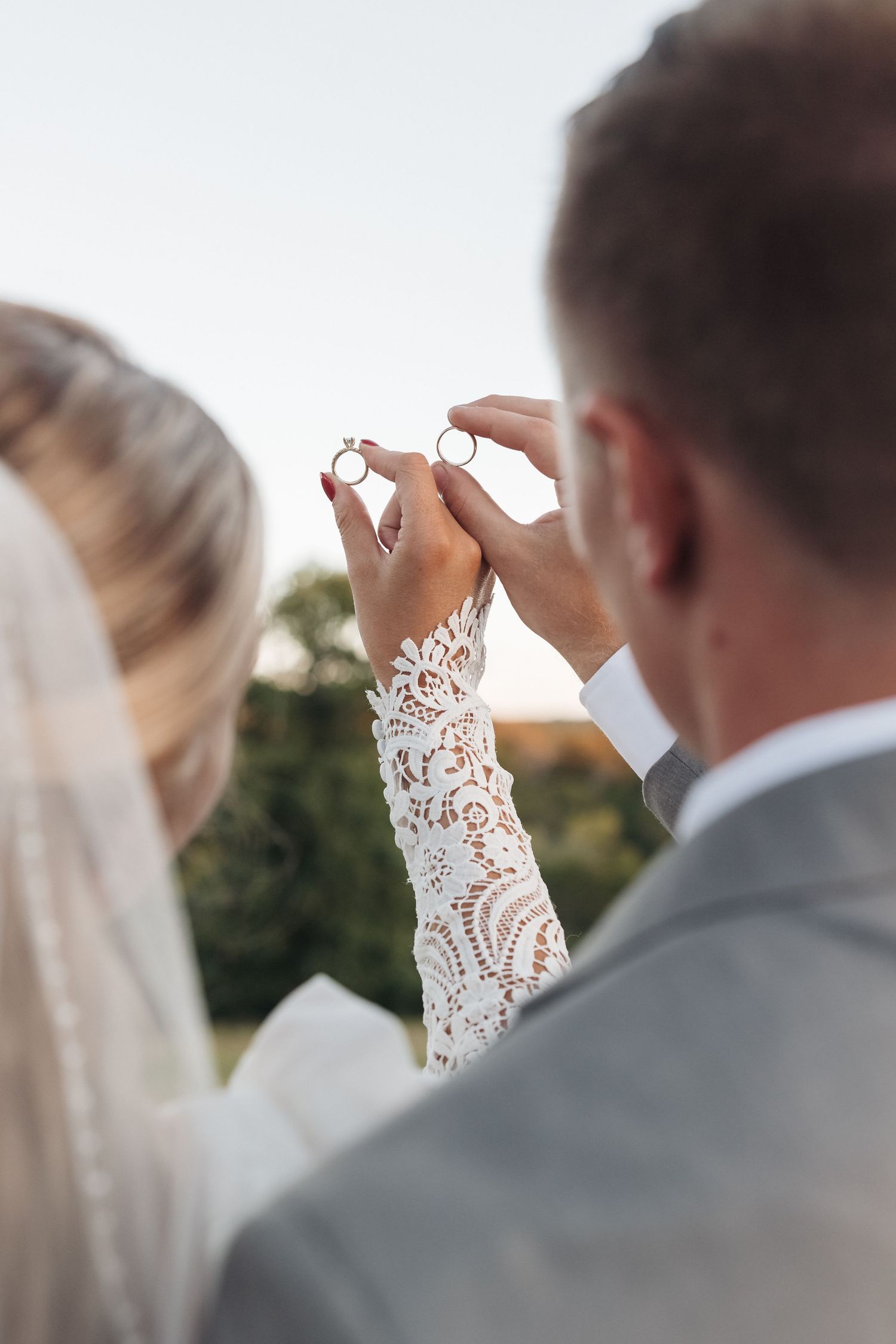 A detailed shot of lace sleeves and wedding rings being exchanged during an outdoor ceremony.