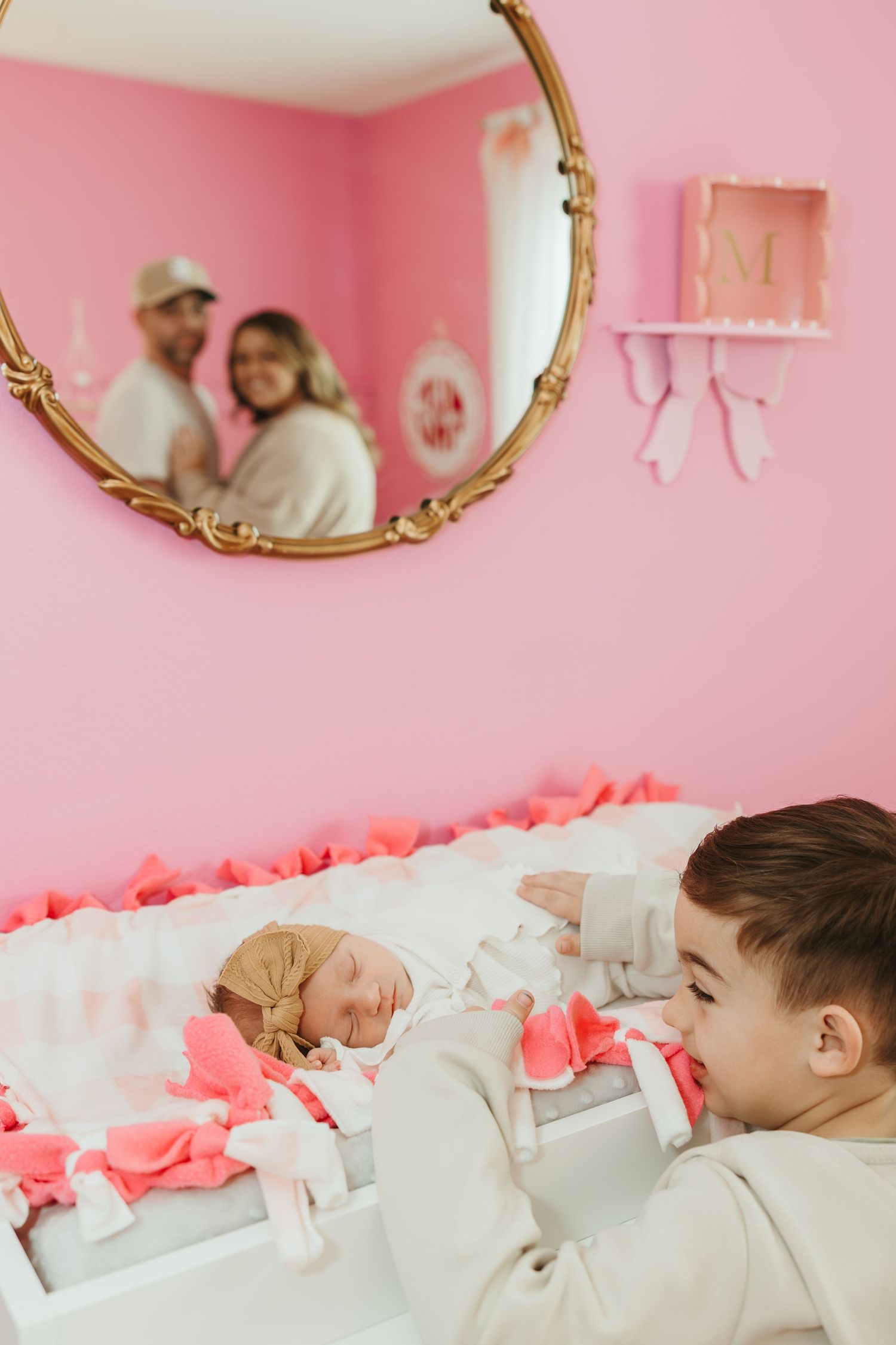 Two people tending to a baby in a crib with pink room decor and coral ribbons along the railing.