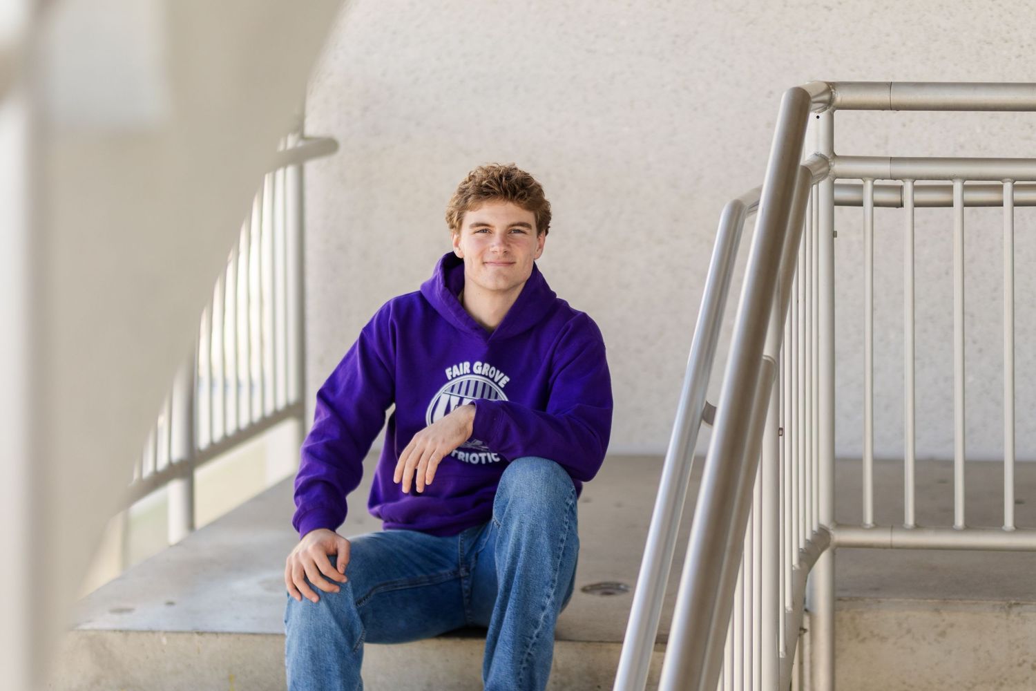 Someone wearing a purple hoodie sits casually on concrete steps near a metal railing.