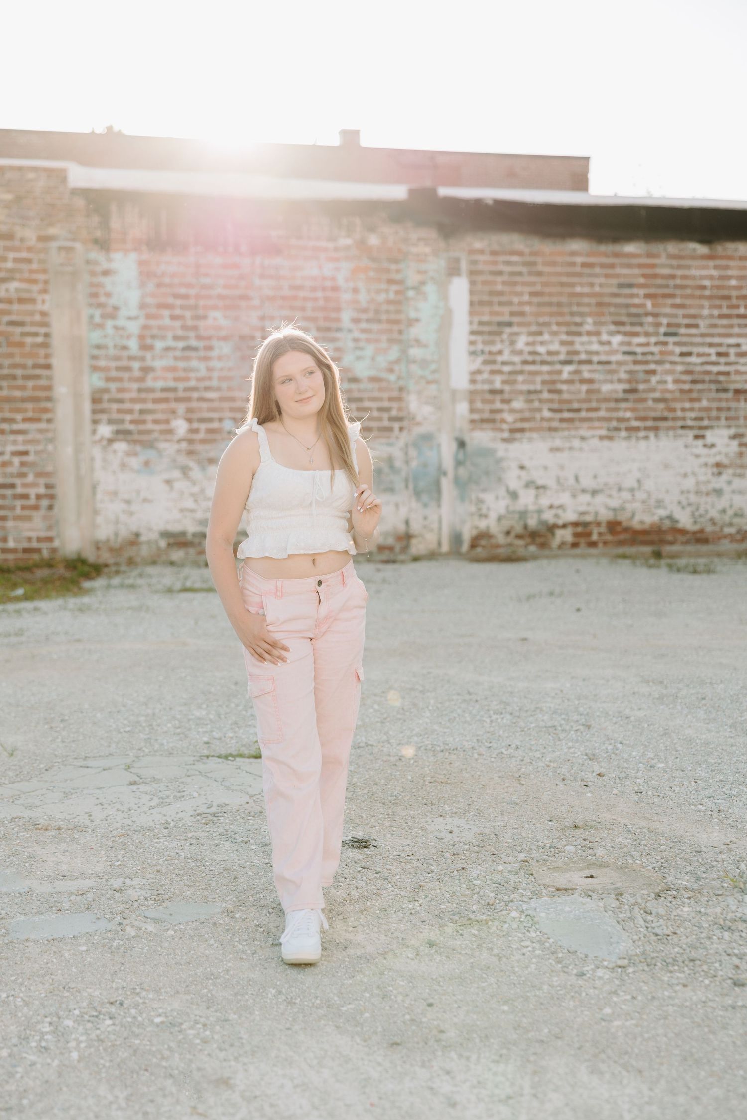 Urban lifestyle portrait showing a person in pink pants and white top posing against a brick wall background.