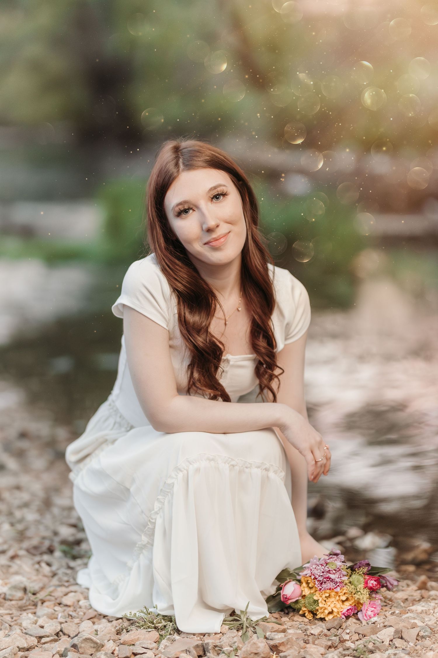 Portrait of a woman in white dress sitting on ground with flowers during golden hour.