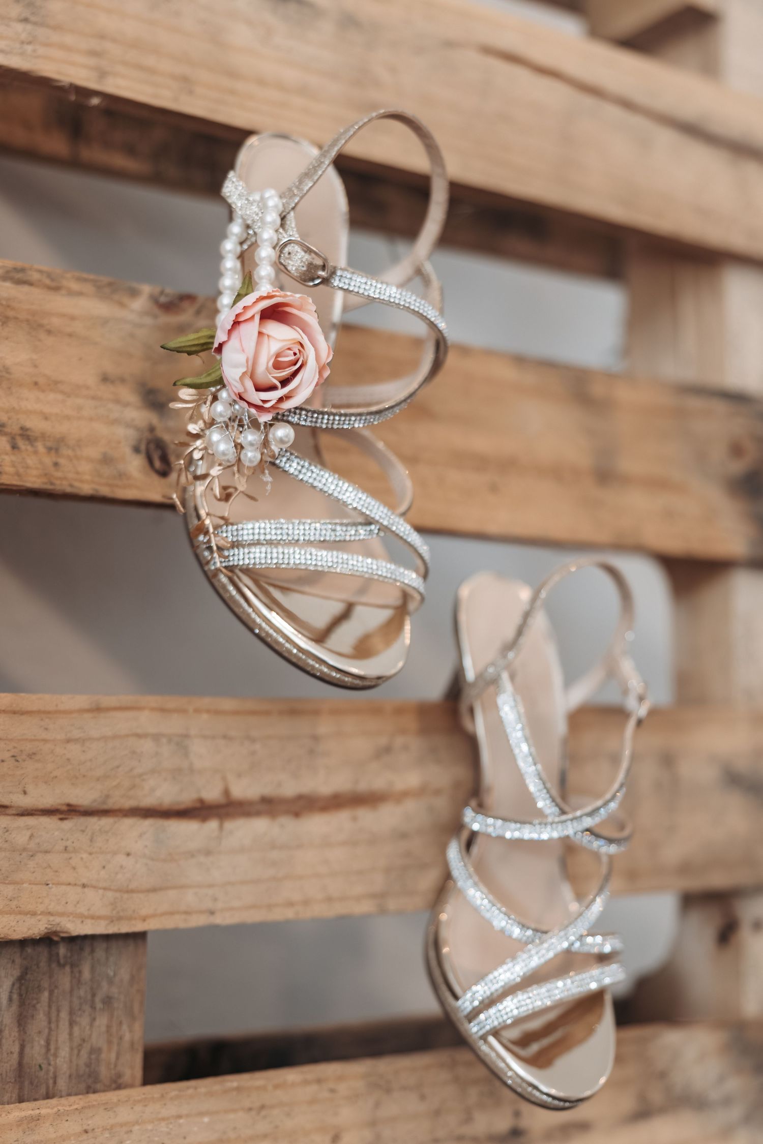 Elegant bridal sandals with crystal embellishments and a blush rose detail rest on rustic wooden pallets.