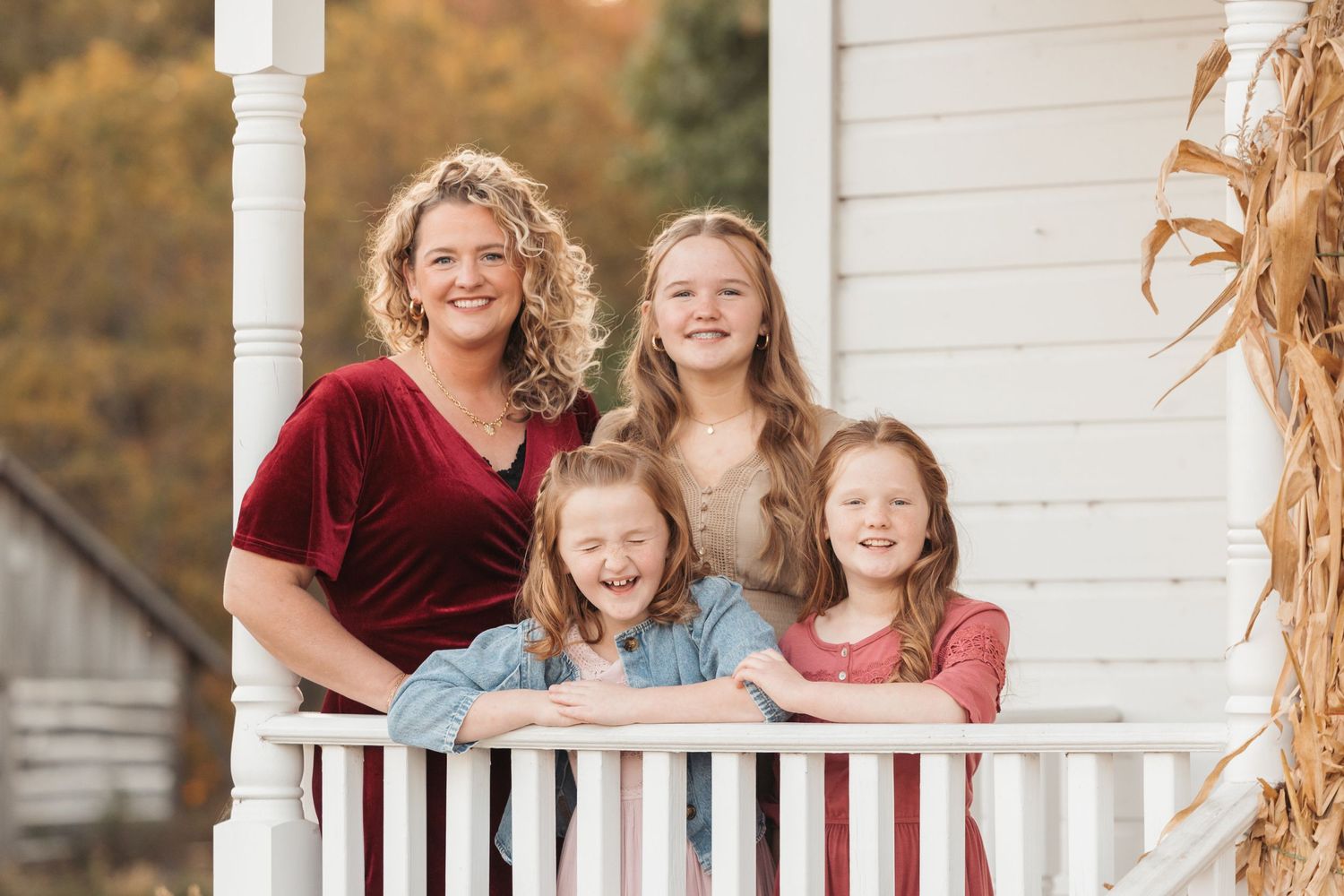 Family group smiling together on white porch with fall decor.