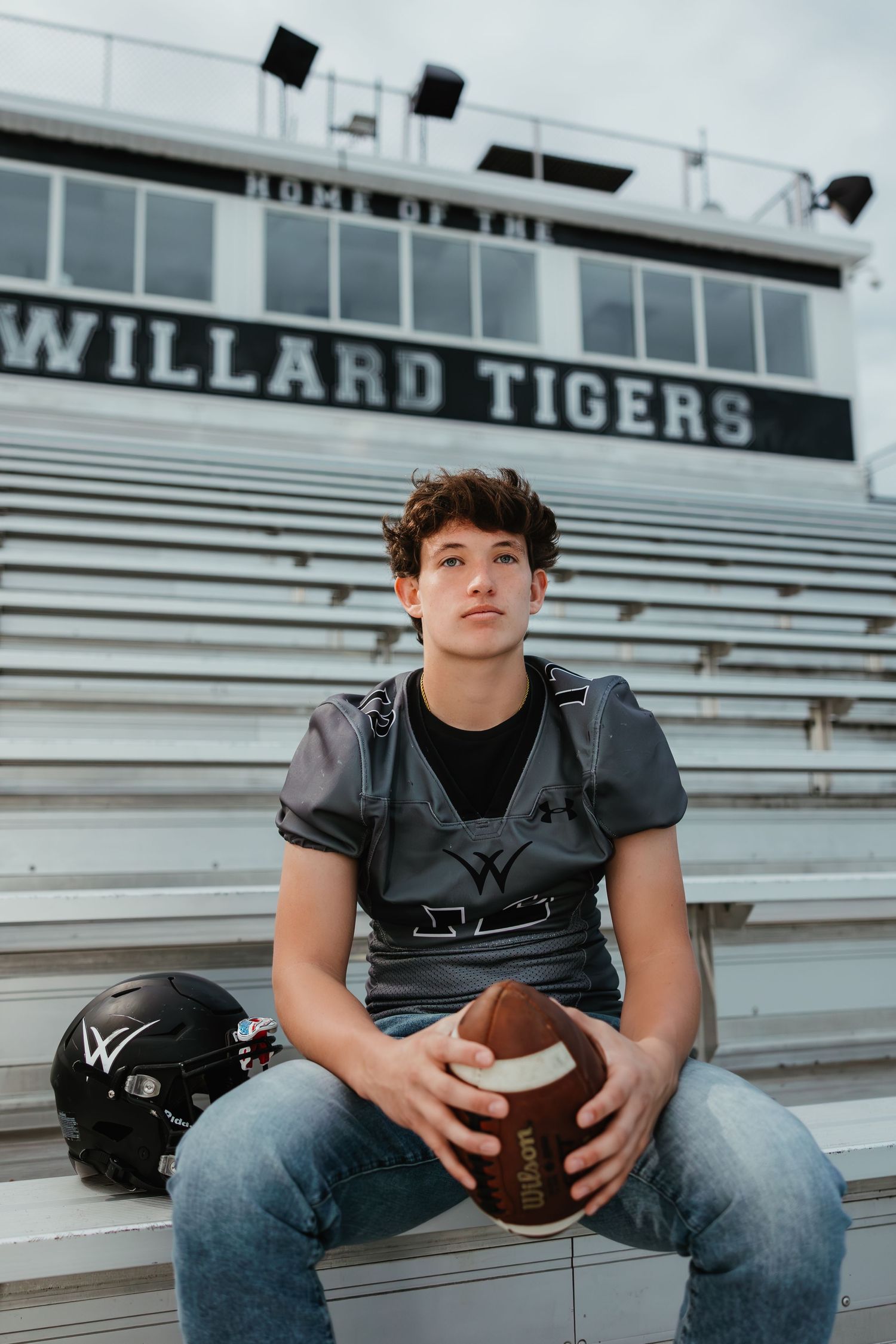 A football player sits on stadium bleachers holding a ball at the Willard Tigers field.