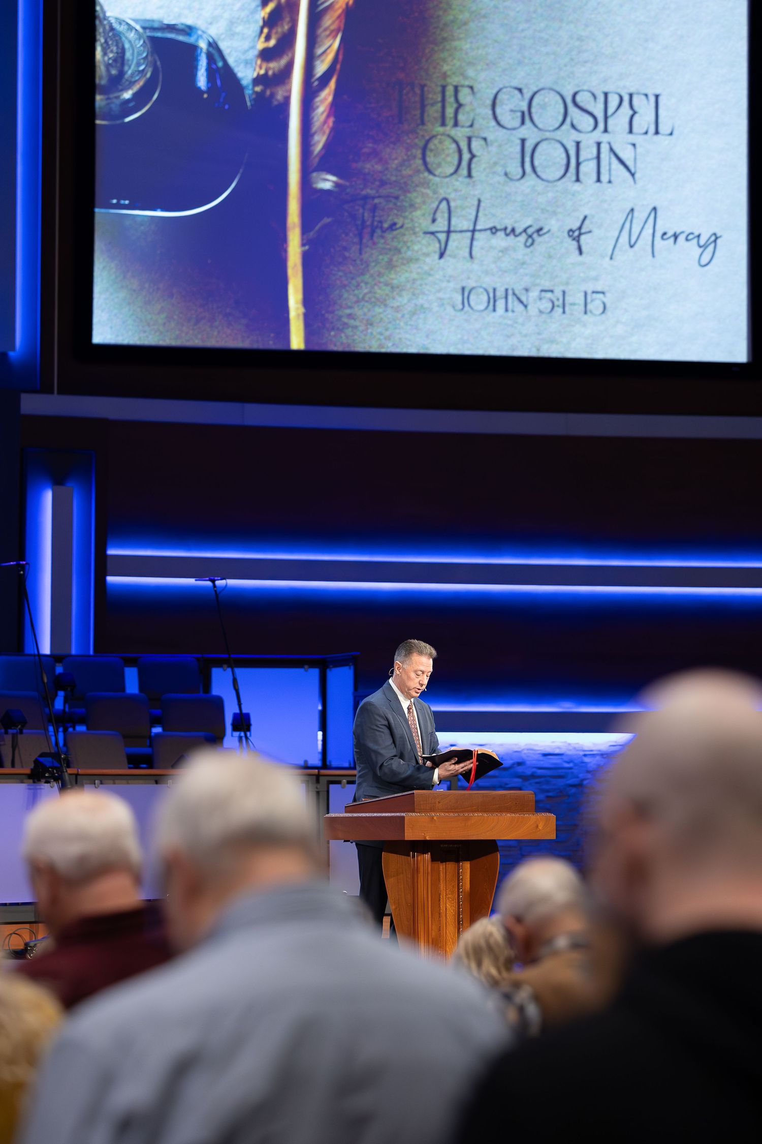 Church service showing Gospel of John scripture displayed on screen above pulpit.