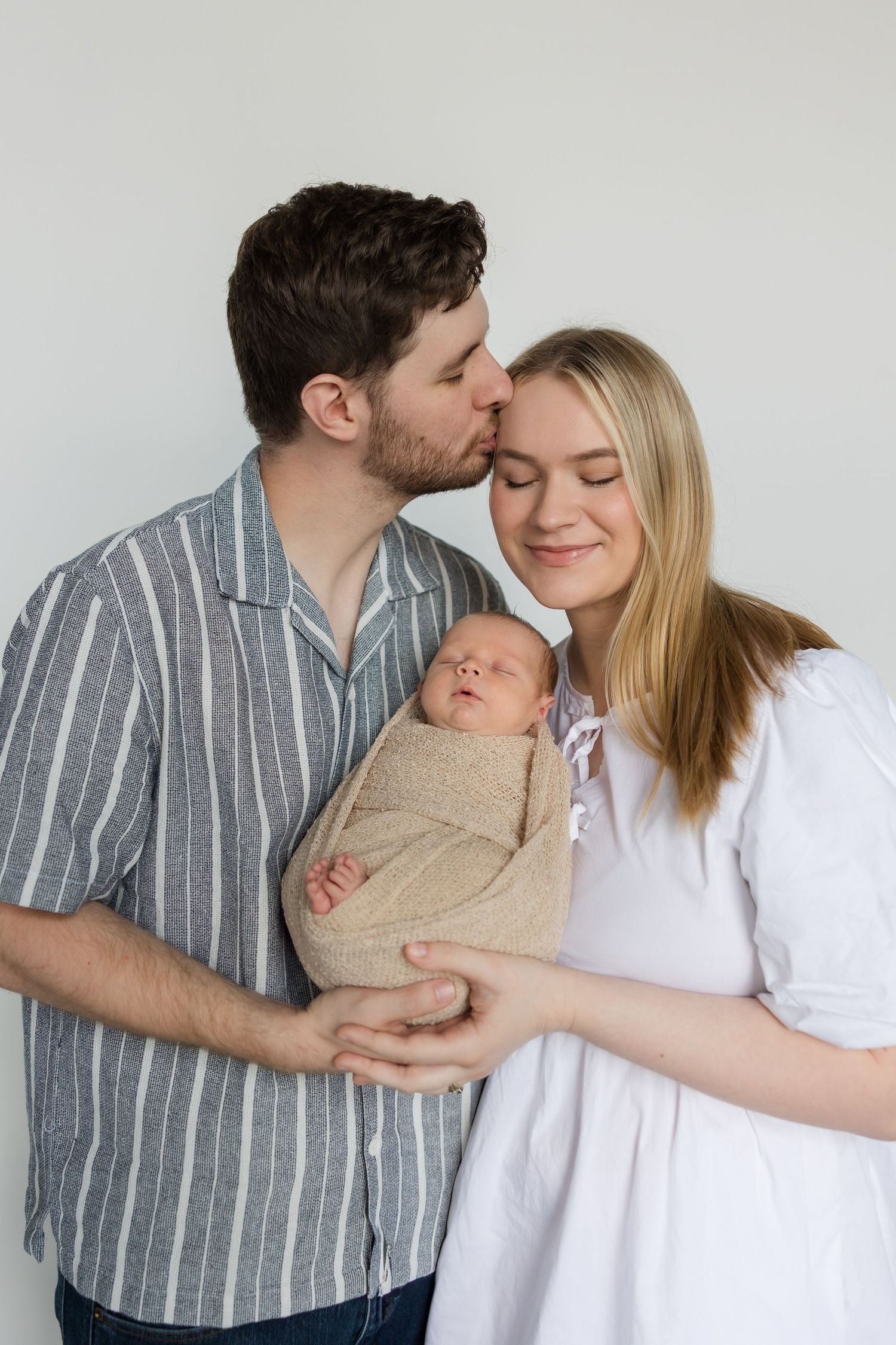 A family of three shares tender moments together in a series of intimate poses against a light backdrop.