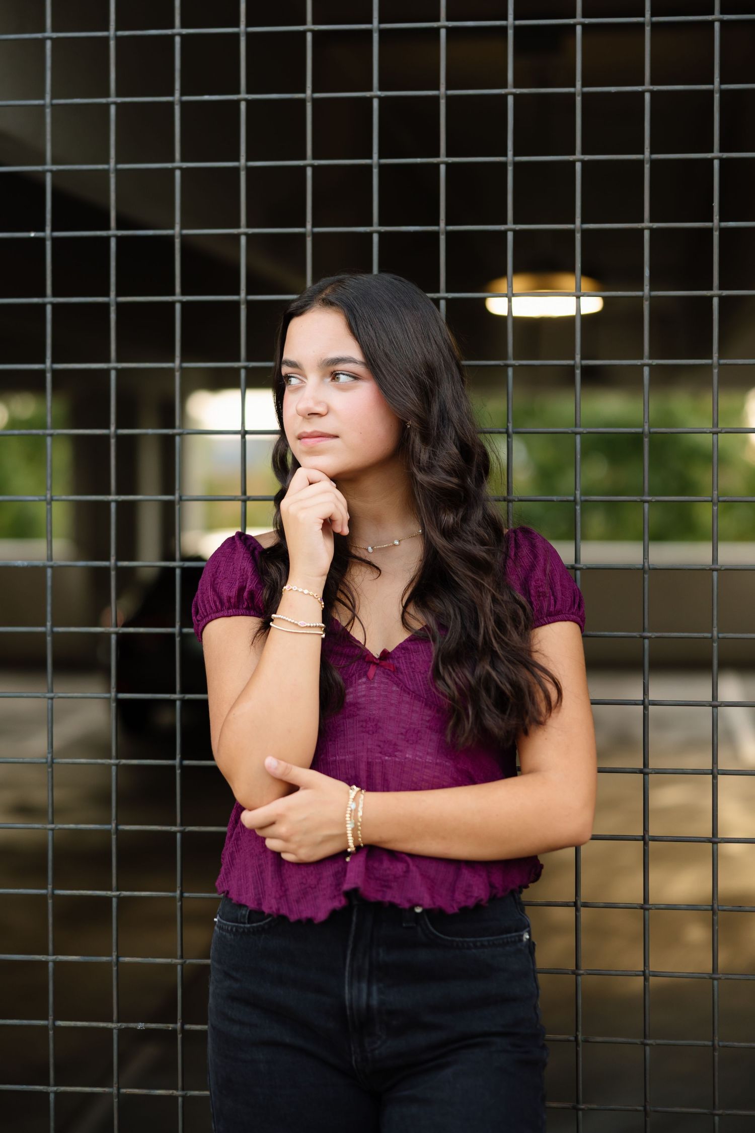 A person in a purple top and dark pants poses thoughtfully against a wire mesh fence in a three-panel photo series.