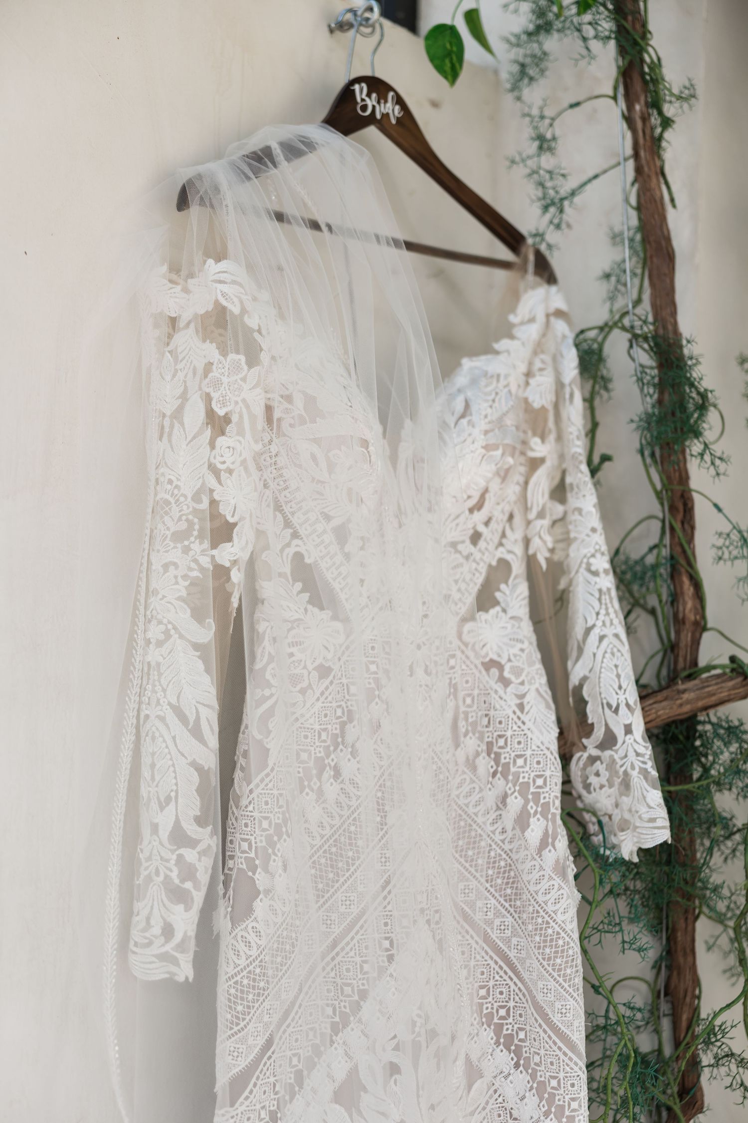 Elegant lace wedding dress with long sleeves and veil hanging on a wooden Bride hanger.
