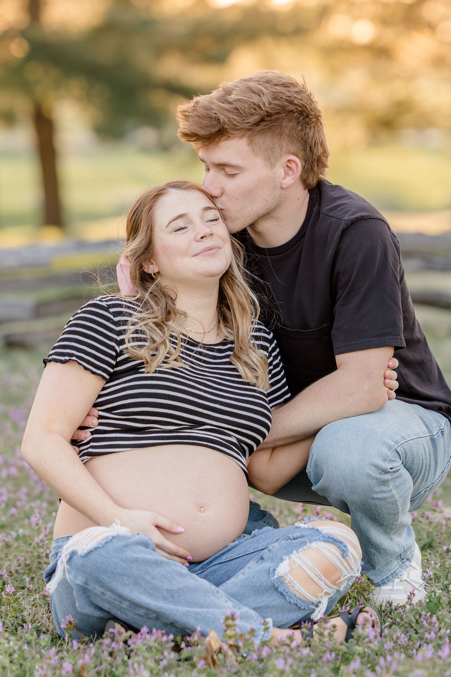 A tender maternity moment outdoors as a couple sits together among wildflowers during a sunset photo session.